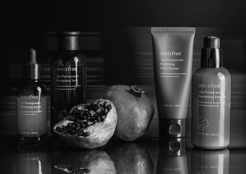 Black and white photo of skincare products with pomegranate and open pomegranate fruit in front.