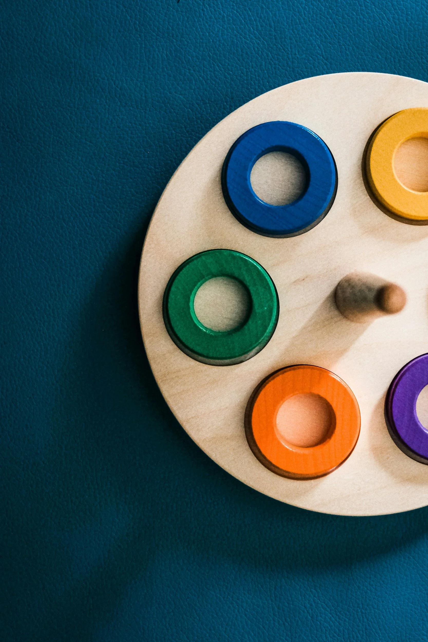 Close-up of a wooden shape sorter toy with colorful circular pieces on a blue textured background.
