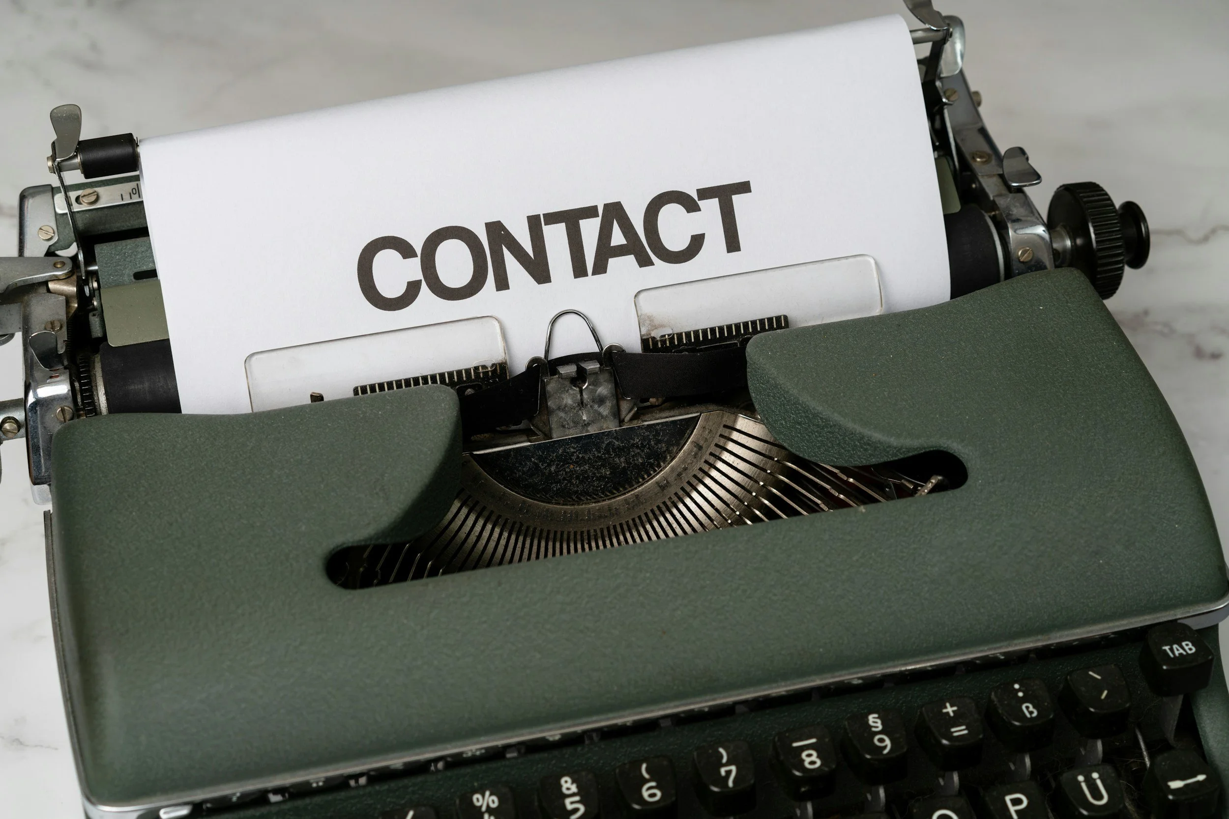 An old typewriter with a paper that has the word 'CONTACT' printed on it.