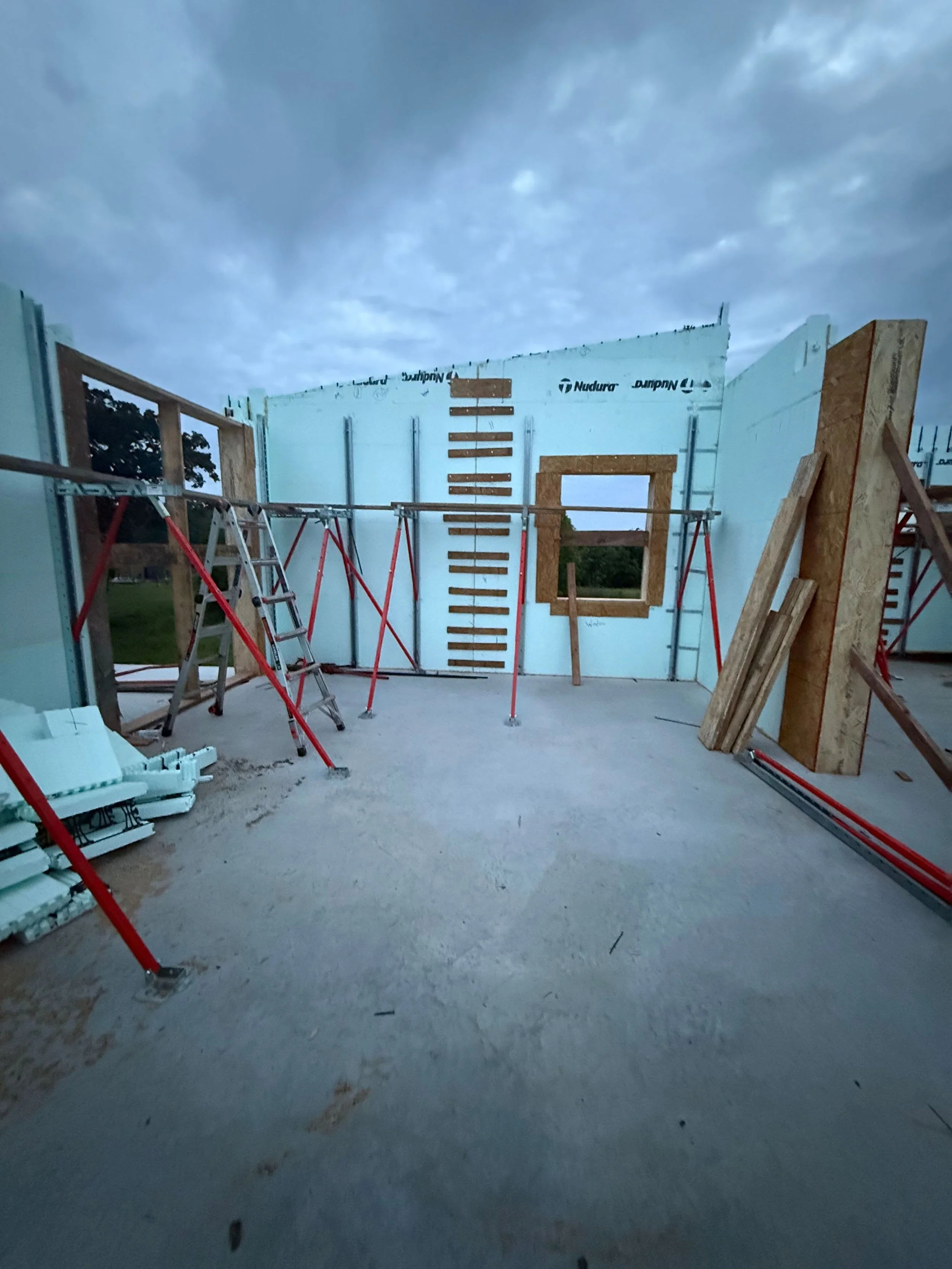 Construction site with partially built walls, ladders, and wooden frames under a cloudy sky.