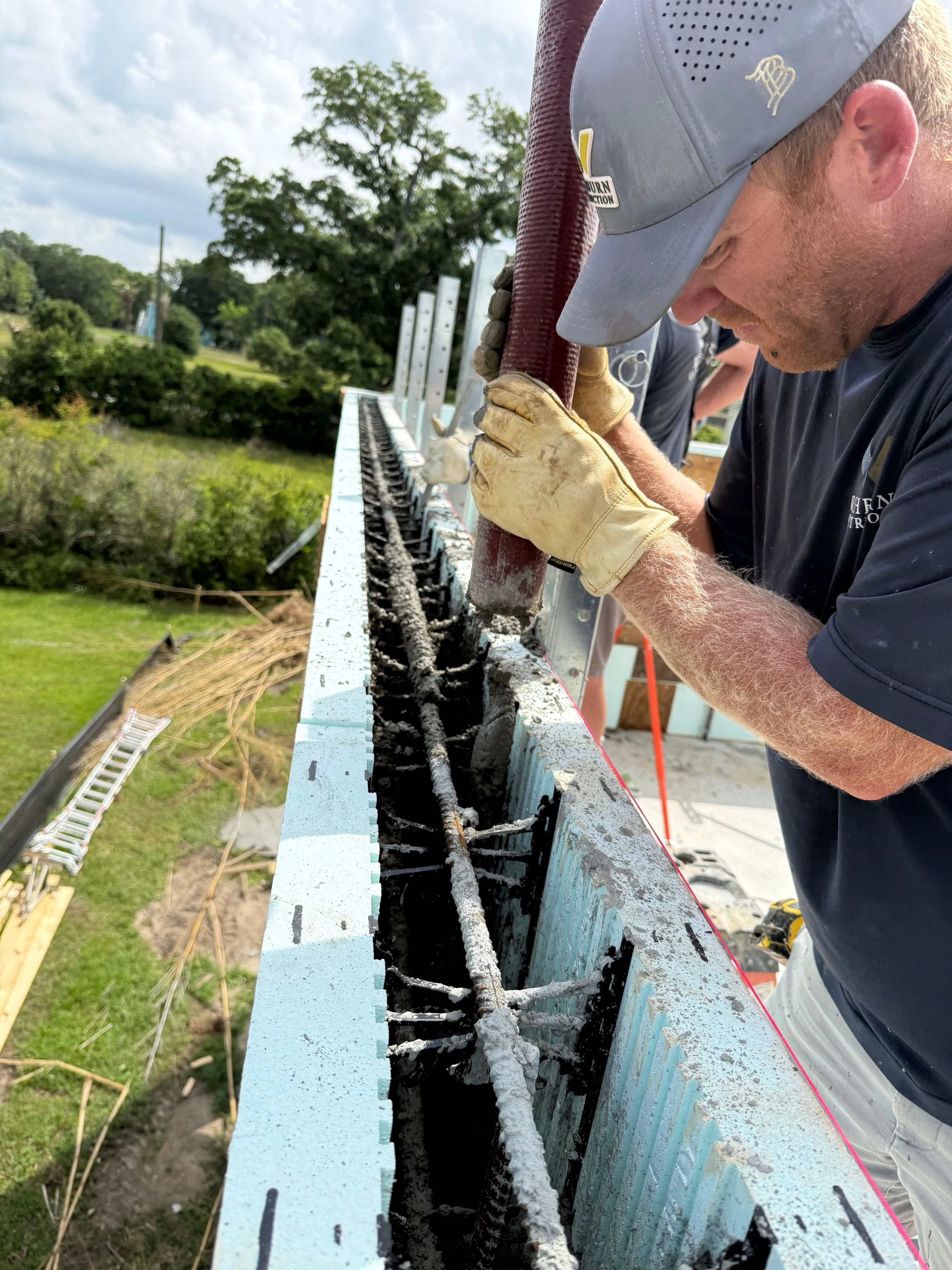 Worker inspecting rebar in a concrete wall during construction, with tools and a green outdoor landscape in the background.
