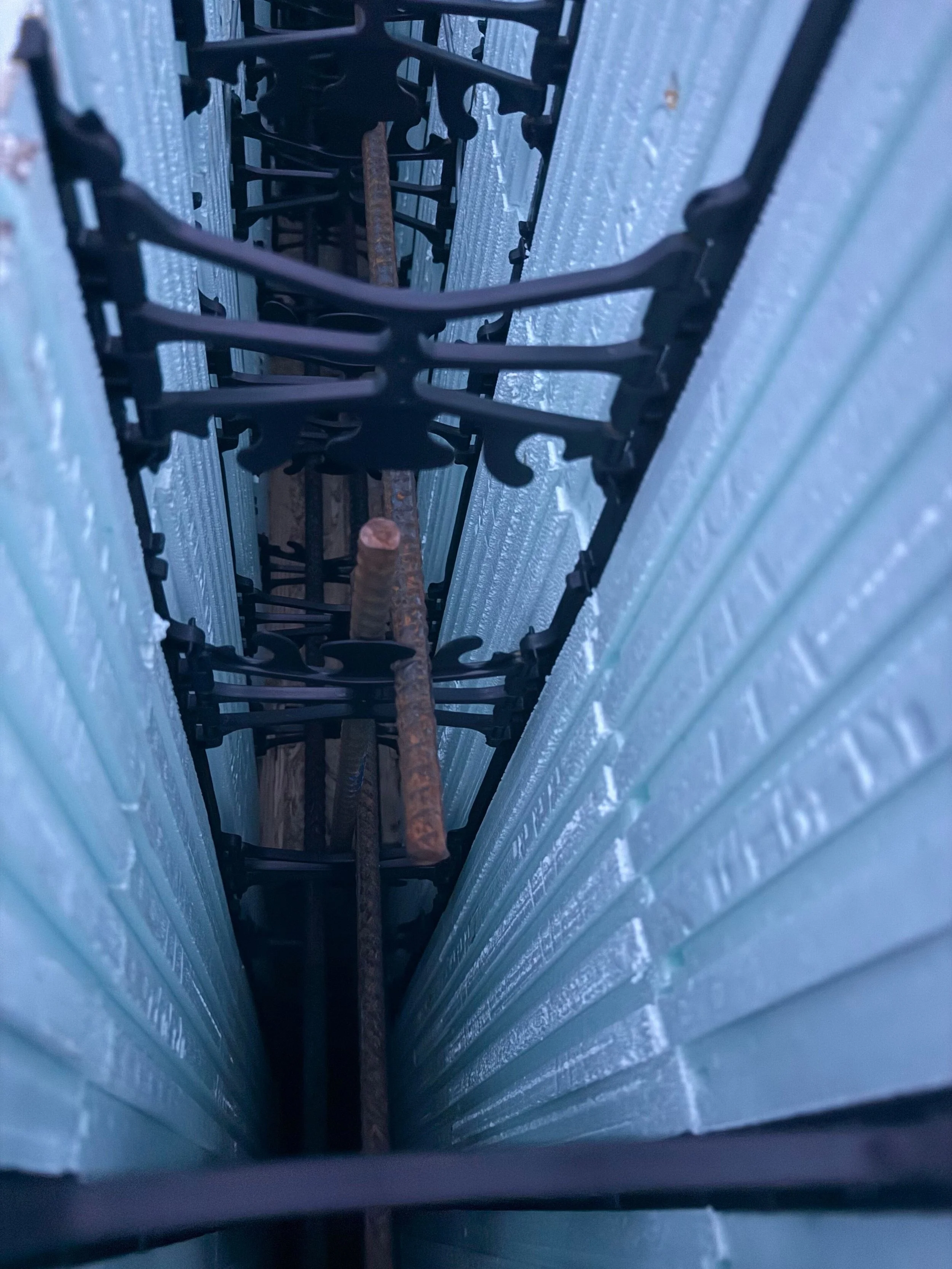 Looking down a narrow gap between two corrugated metal walls, with a rusty metal bar running through the center.