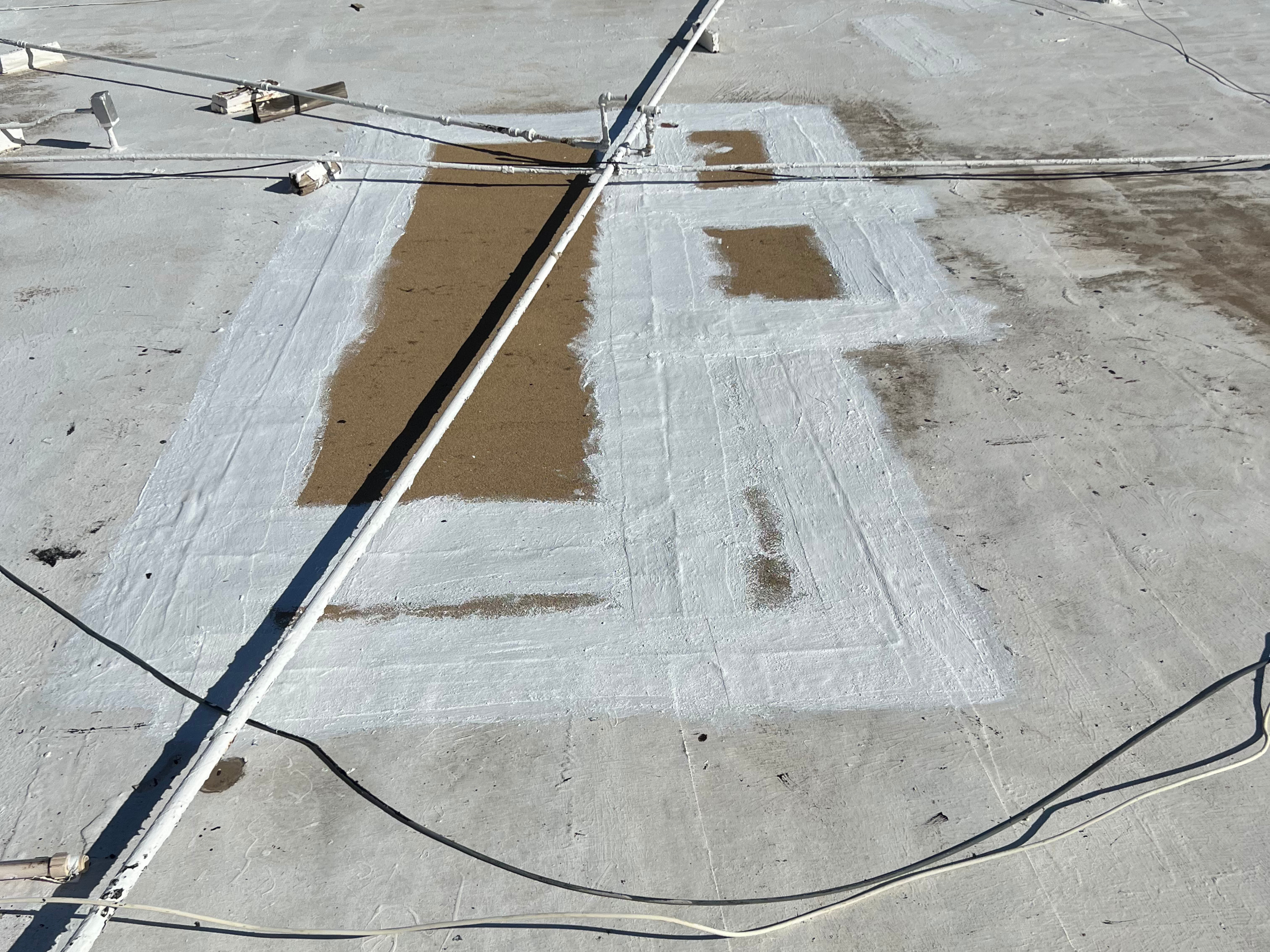 A rooftop with white sealant or coating, electrical wires, and pipes.