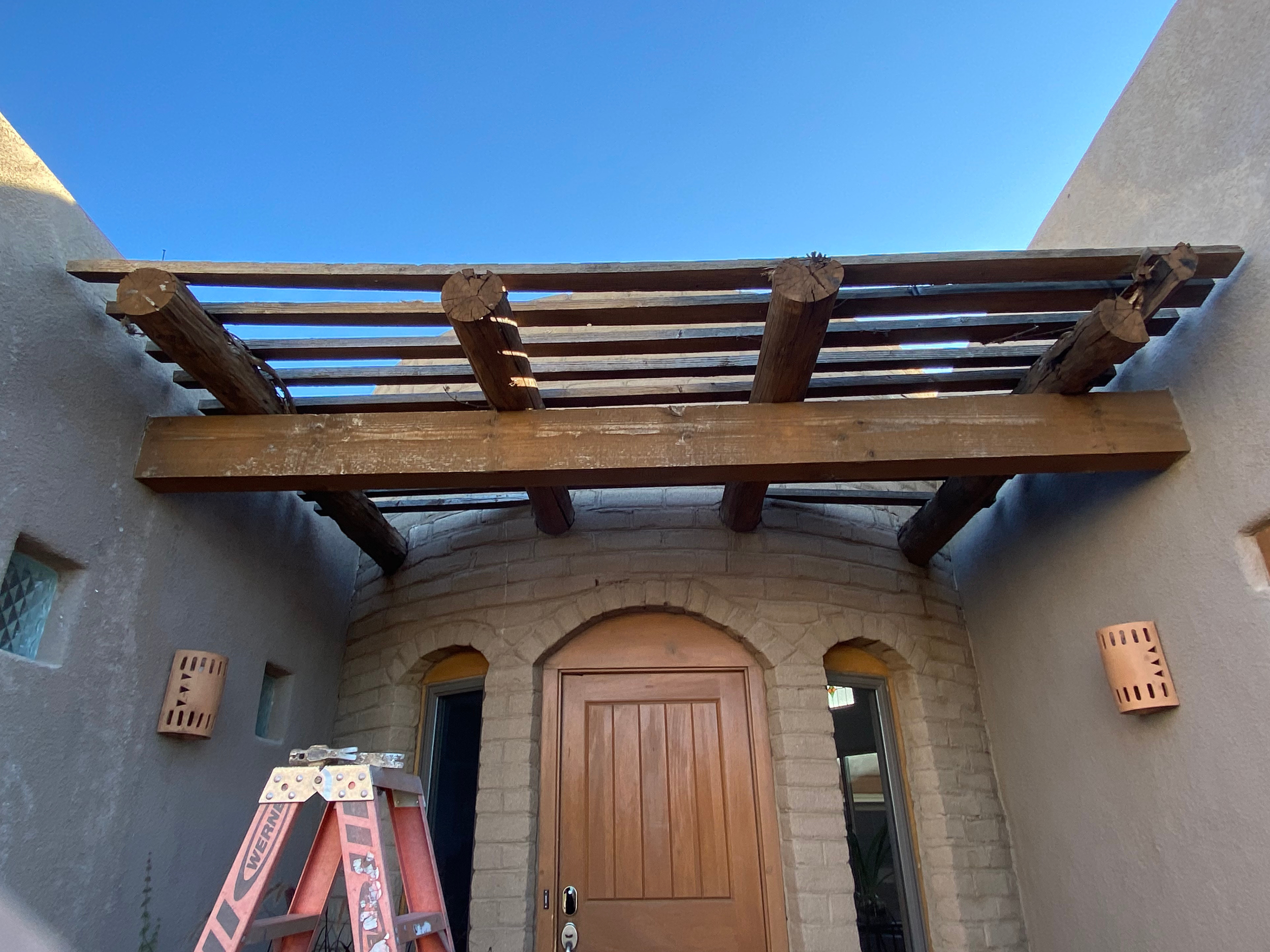 Construction ladder inside a building, HVAC vents on the wall, a wooden door, and an unfinished ceiling with wooden beams.
