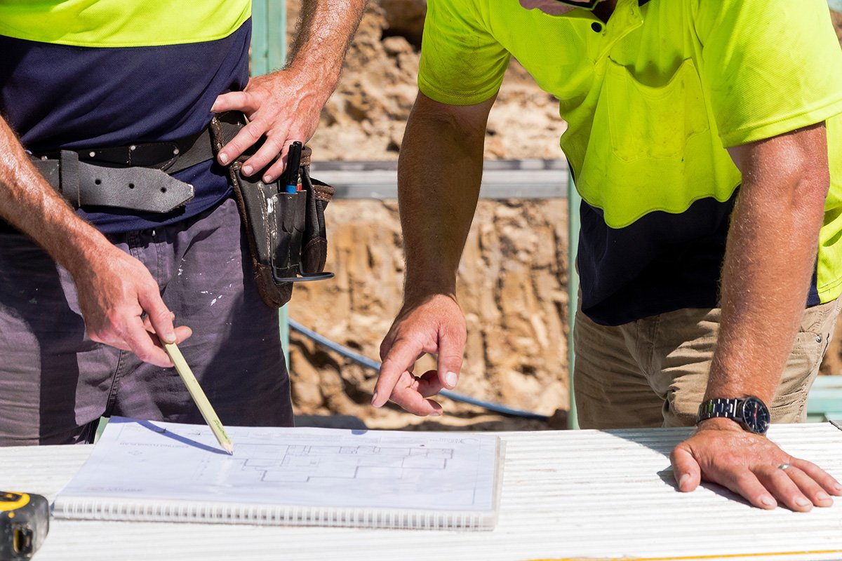 Two construction workers reviewing blueprints at a job site.