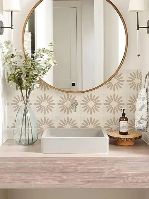 Bathroom vanity with a round mirror, white vessel sink, vase with greenery, soap dispenser, and decorative towel holder with a floral towel.