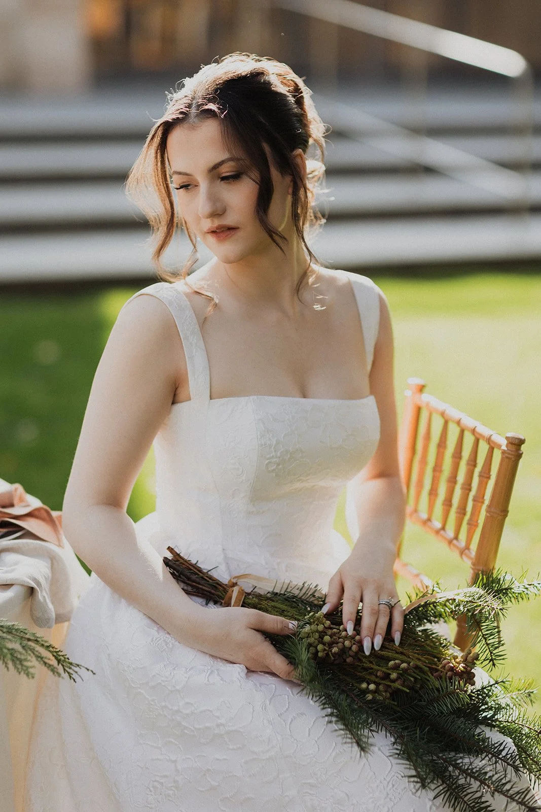 A woman in a white dress holding a small bouquet of greenery outdoors during daytime.