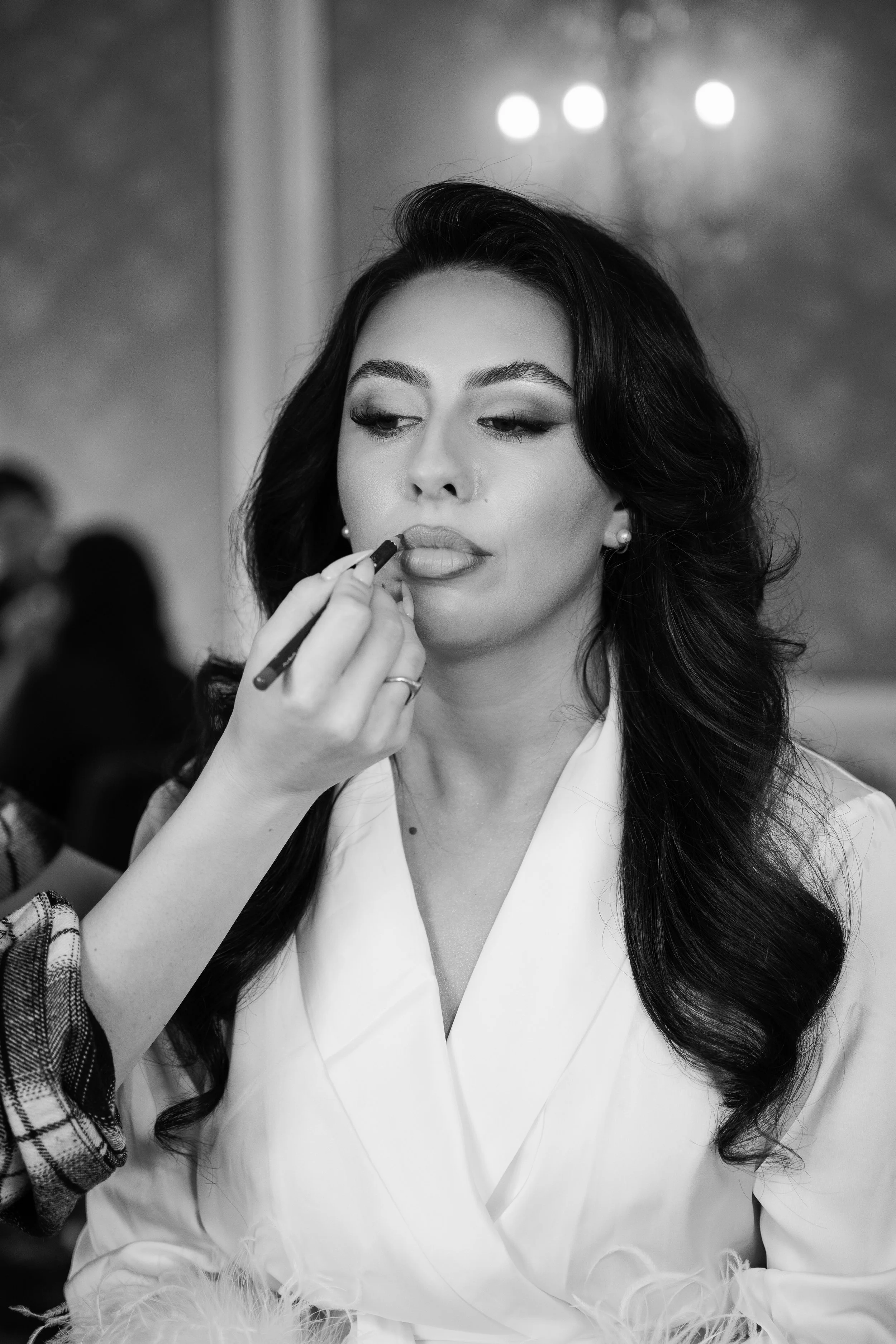 A woman with long dark hair getting her lips painted by another person.