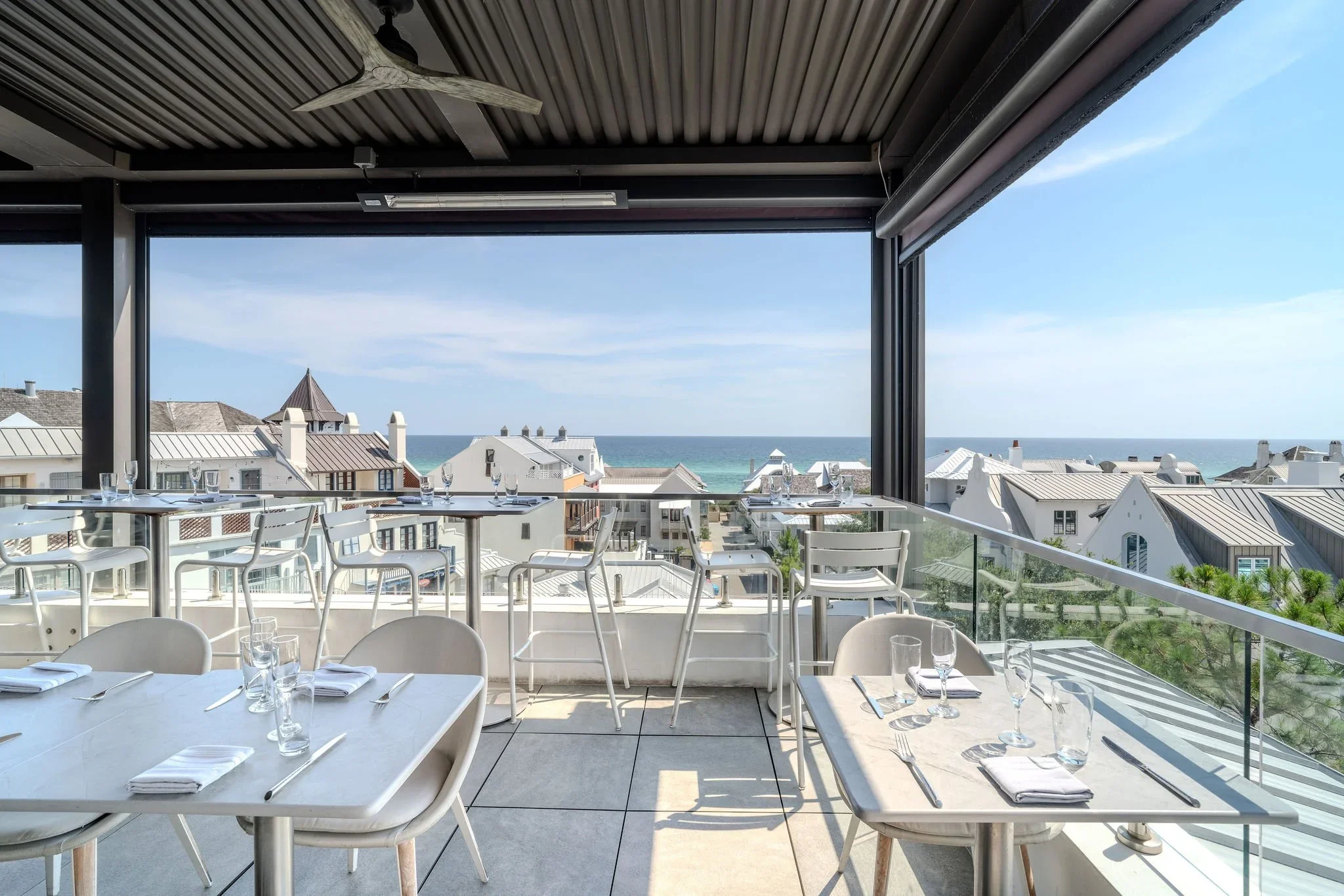 A dining area on a balcony with views of rooftops, the ocean, and sky.