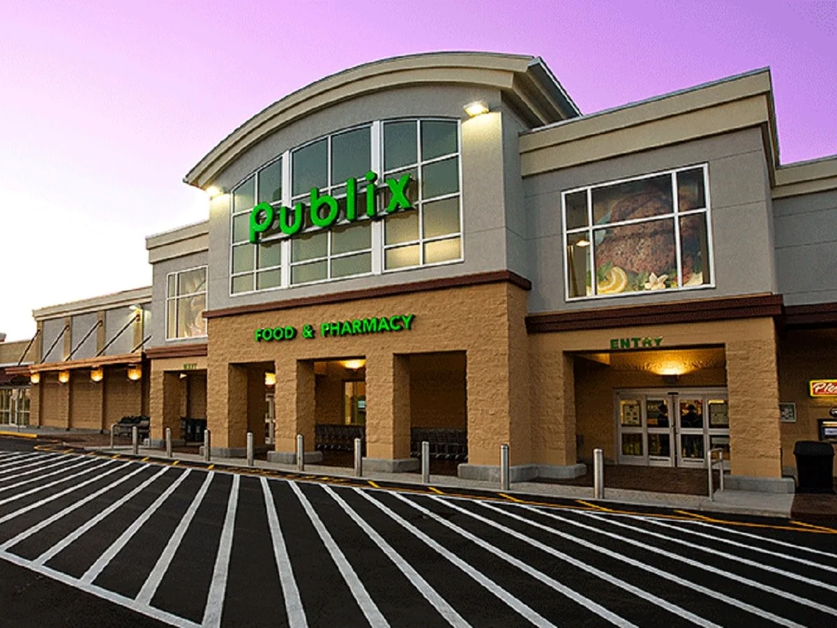 Front view of a Publix grocery store with a large green sign, a designated entrance, and a parking lot in the foreground during dusk.