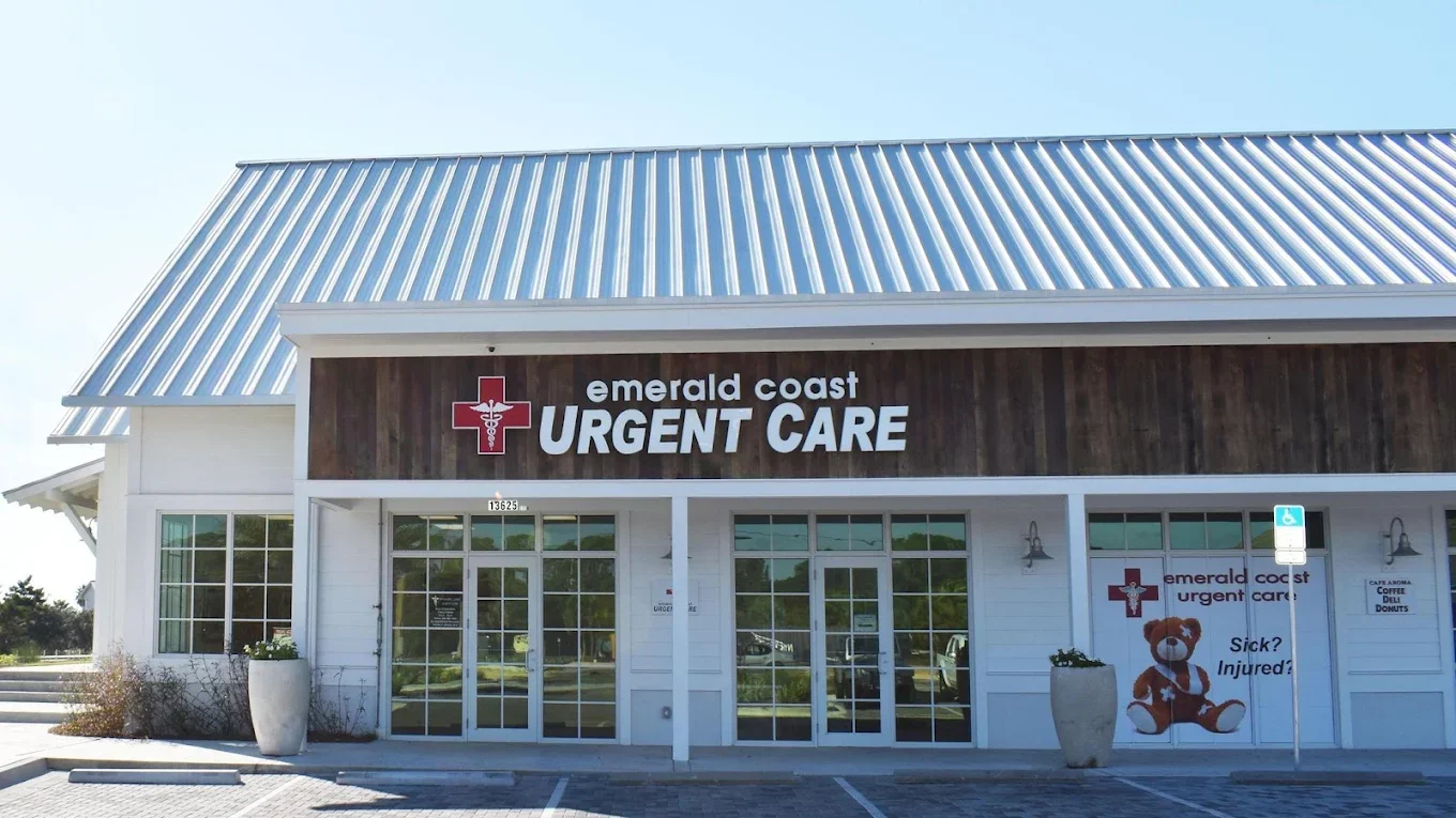 Exterior of Emerald Coast Urgent Care building with signage, glass doors, planters, and a teddy bear in a window
