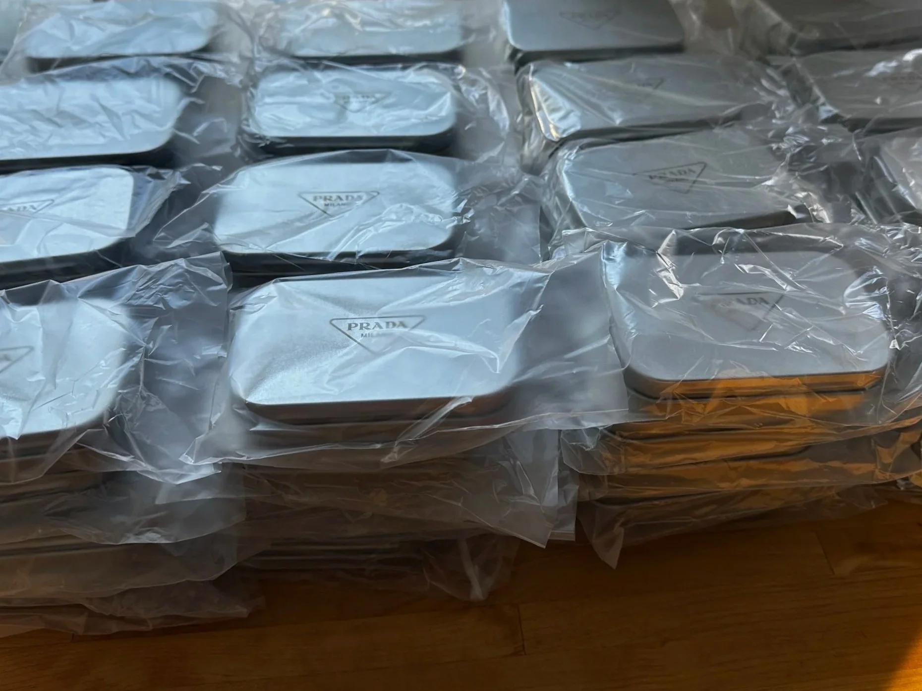 Multiple Prada Milano wallets wrapped in plastic, placed on a wooden surface.