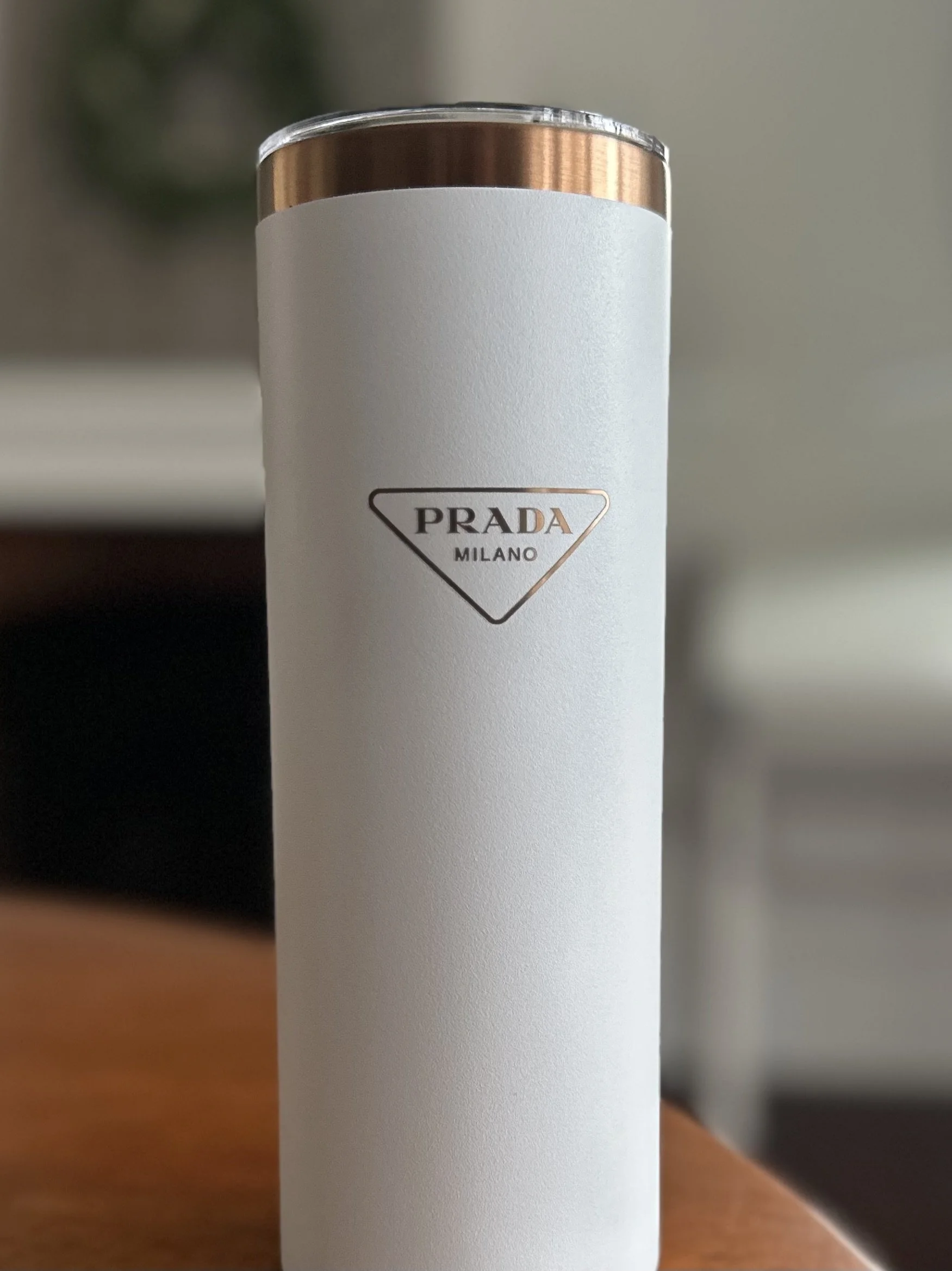 A white insulated tumbler with a copper-colored lid and a blank white label, standing on a wooden surface.