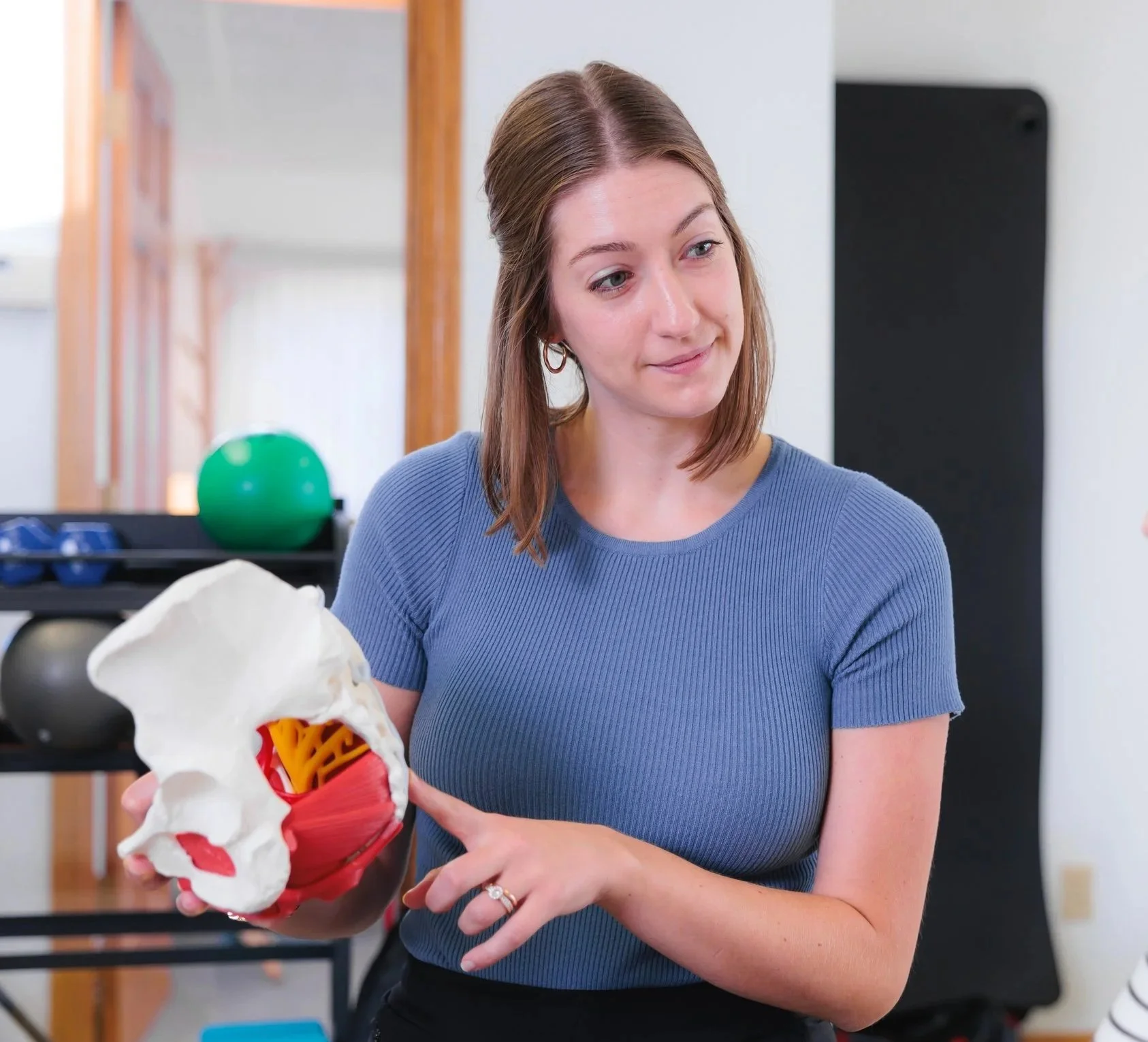 Pelvic health physical therapist using a pelvic model to explain bowel concerns and pelvic floor function at Cultivate Your Wellbeing, serving Mequon and Brookfield, Wisconsin.