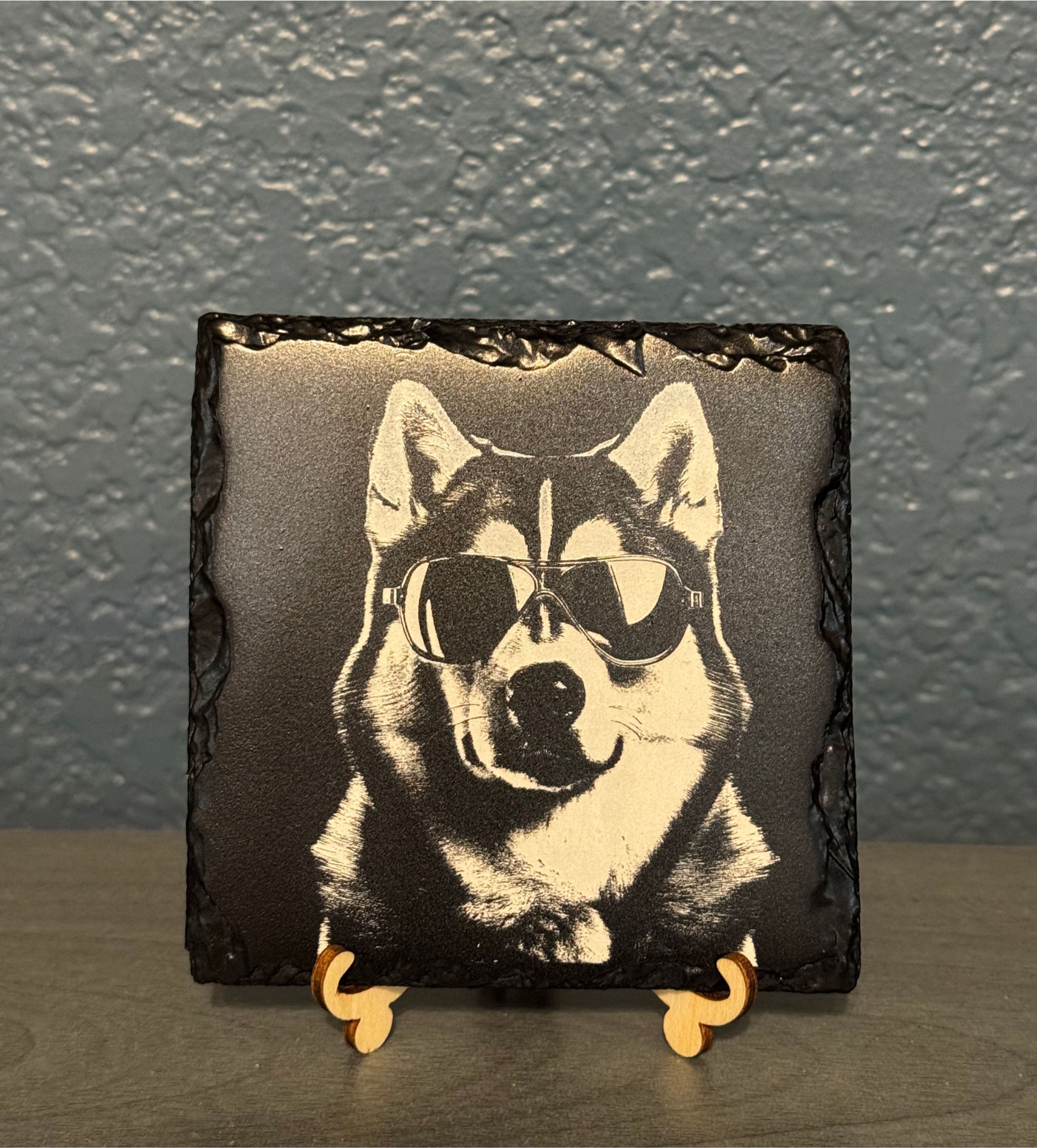 A framed illustration of a Siberian Husky dog wearing sunglasses, mounted on a small wooden stand.