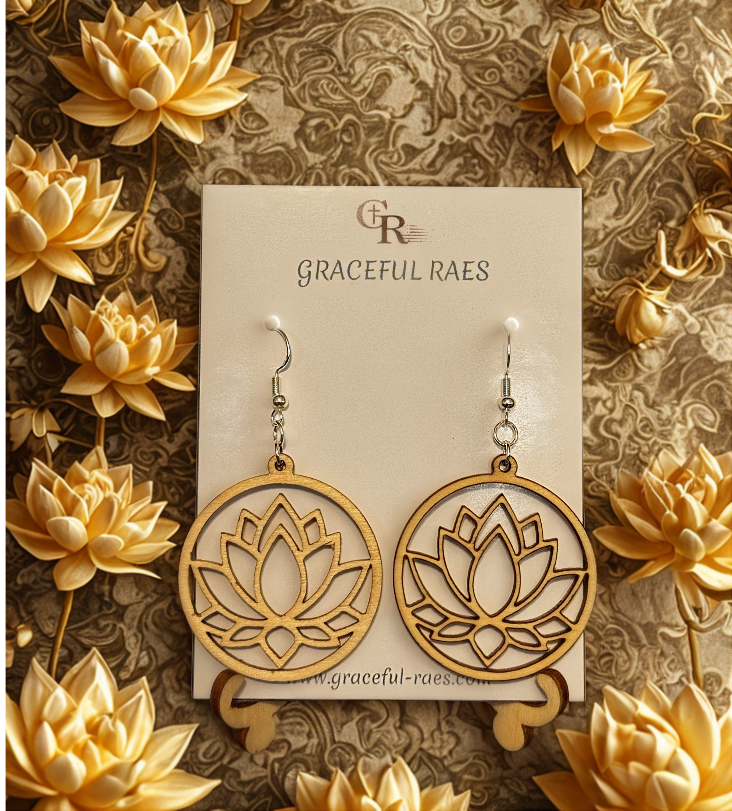 A jewelry display featuring wooden earrings with intricate floral designs, surrounded by decorative yellow flowers on a textured background, with a sign that reads "Graceful Raes" and the website "www.graceful-raes.com".