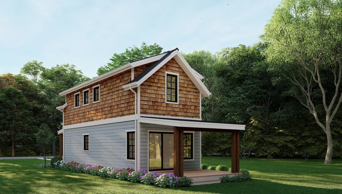 A two-story house with a wooden shingle upper exterior, gray lower exterior, black window frames, and a small covered porch, surrounded by green trees and a flower bed.