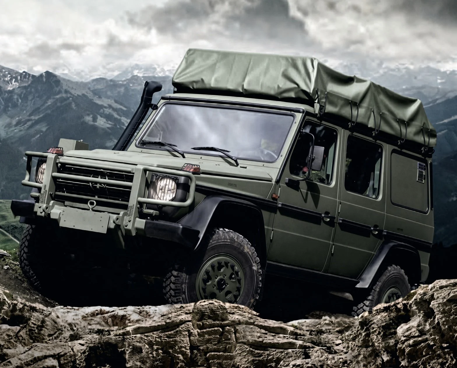 A military green off-road vehicle parked on rocky terrain with mountains in the background