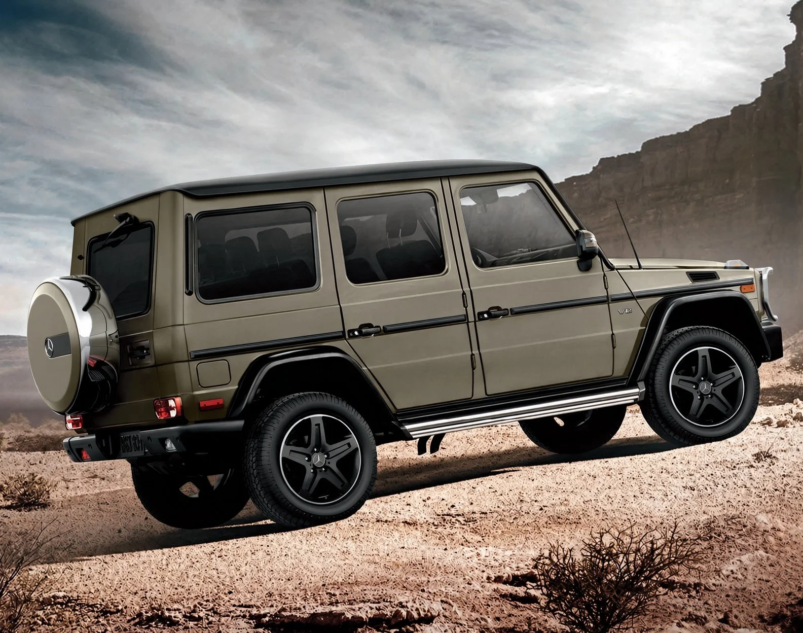 A beige Mercedes-Benz G-Class SUV parked on a desert terrain with rocky cliffs and cloudy sky in the background.