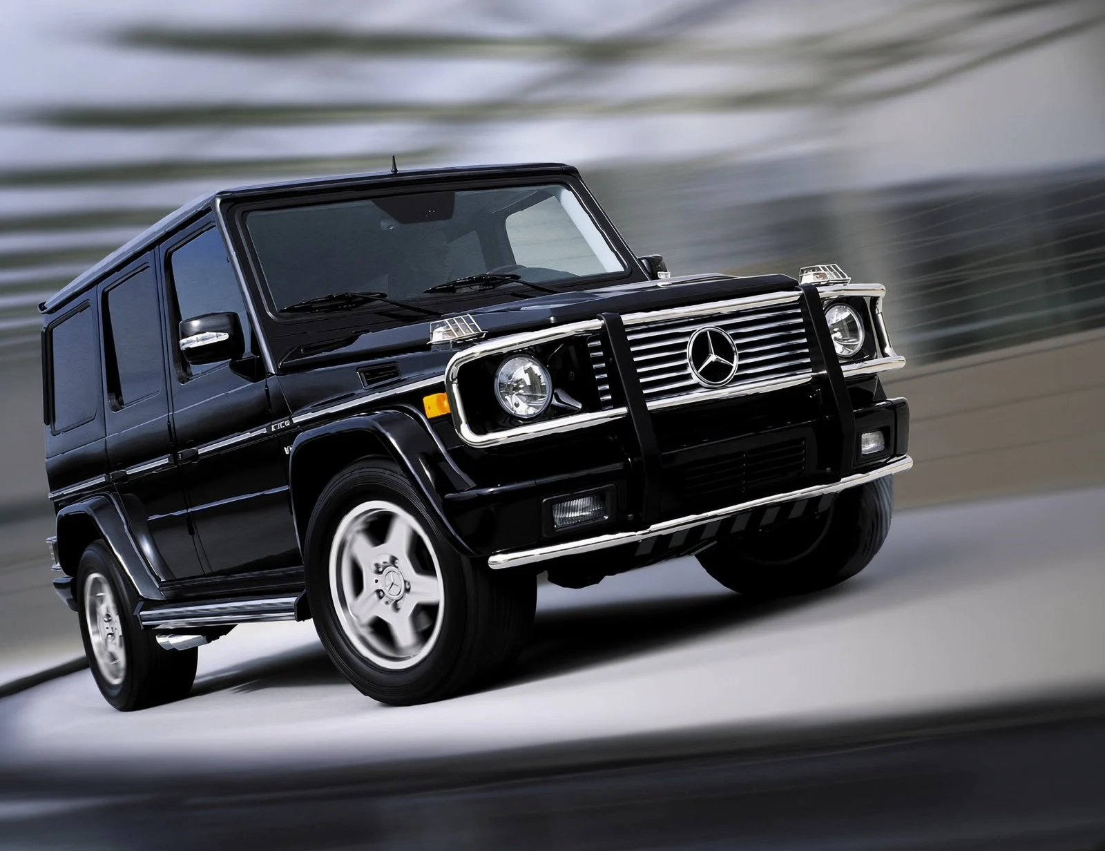 A black Mercedes-Benz G-Class SUV driving on a road, slightly tilted to the right, with a blurred background indicating motion.