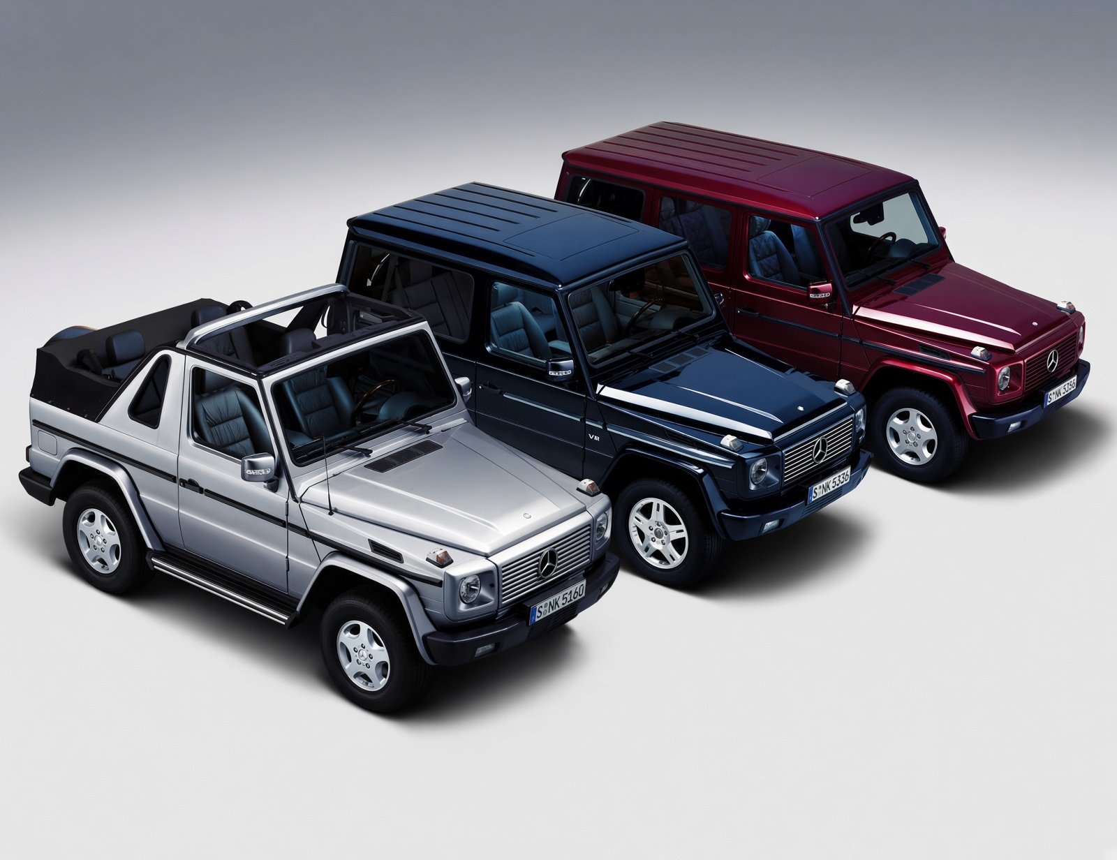 Three Mercedes-Benz G-Class vehicles in silver, dark blue, and maroon parked on a plain surface.