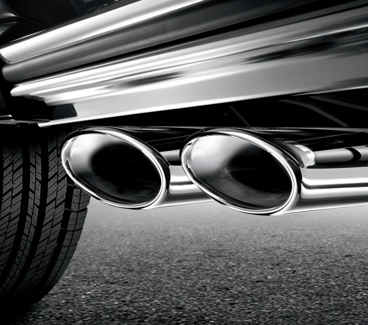 Close-up of two chrome exhaust pipes on a car, with a tire and asphalt ground visible.