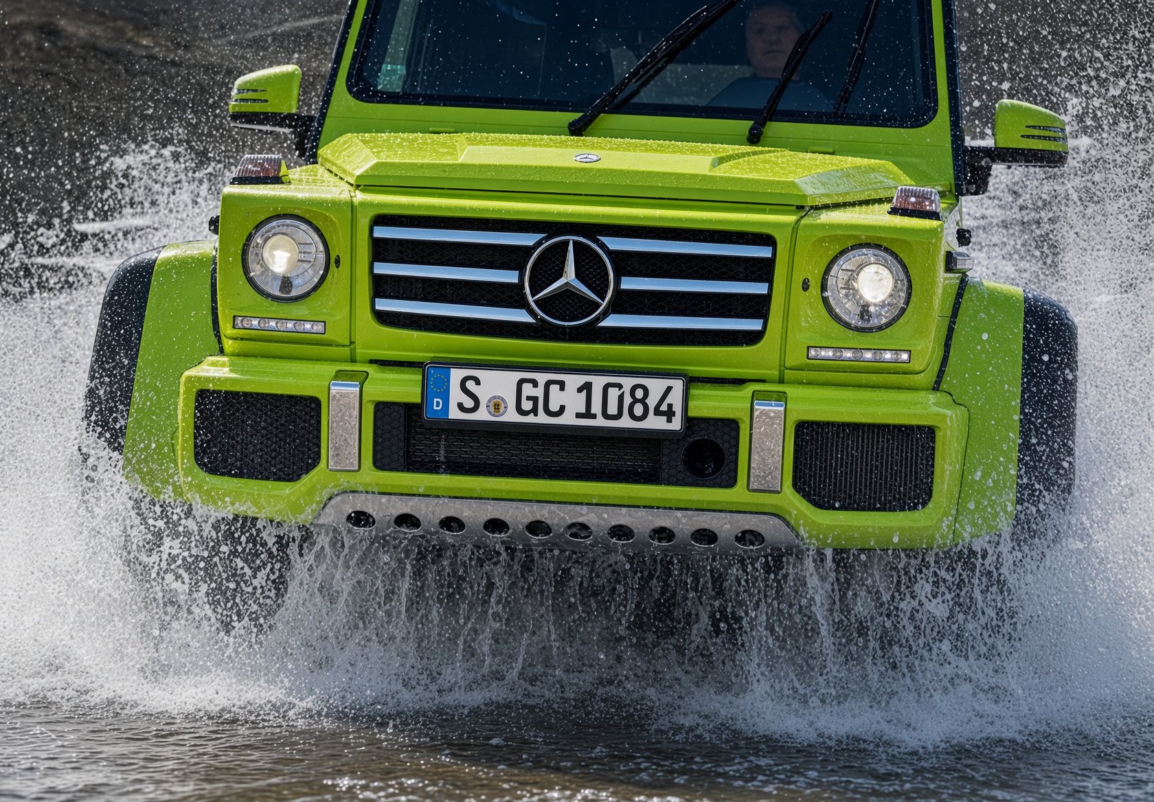 A bright green Mercedes-Benz G-Class luxury SUV driving through water, splashing water around it, with a driver visible through the windshield.