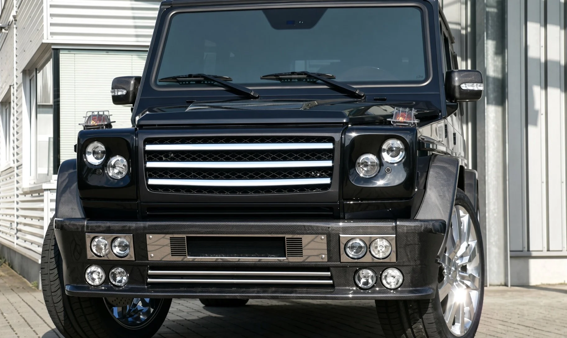 Front view of a black luxury SUV with a chrome grille and multiple round headlights, parked outside a modern building.