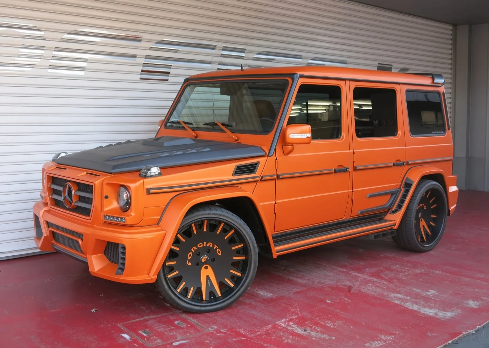 A bright orange Mercedes-Benz G-Class SUV with custom black detailing and wheels, parked in front of a garage door.