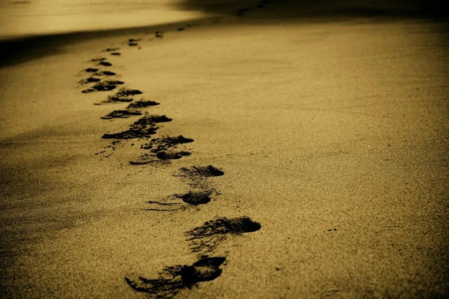 Footprints in the sand on a beach at night or dusk.