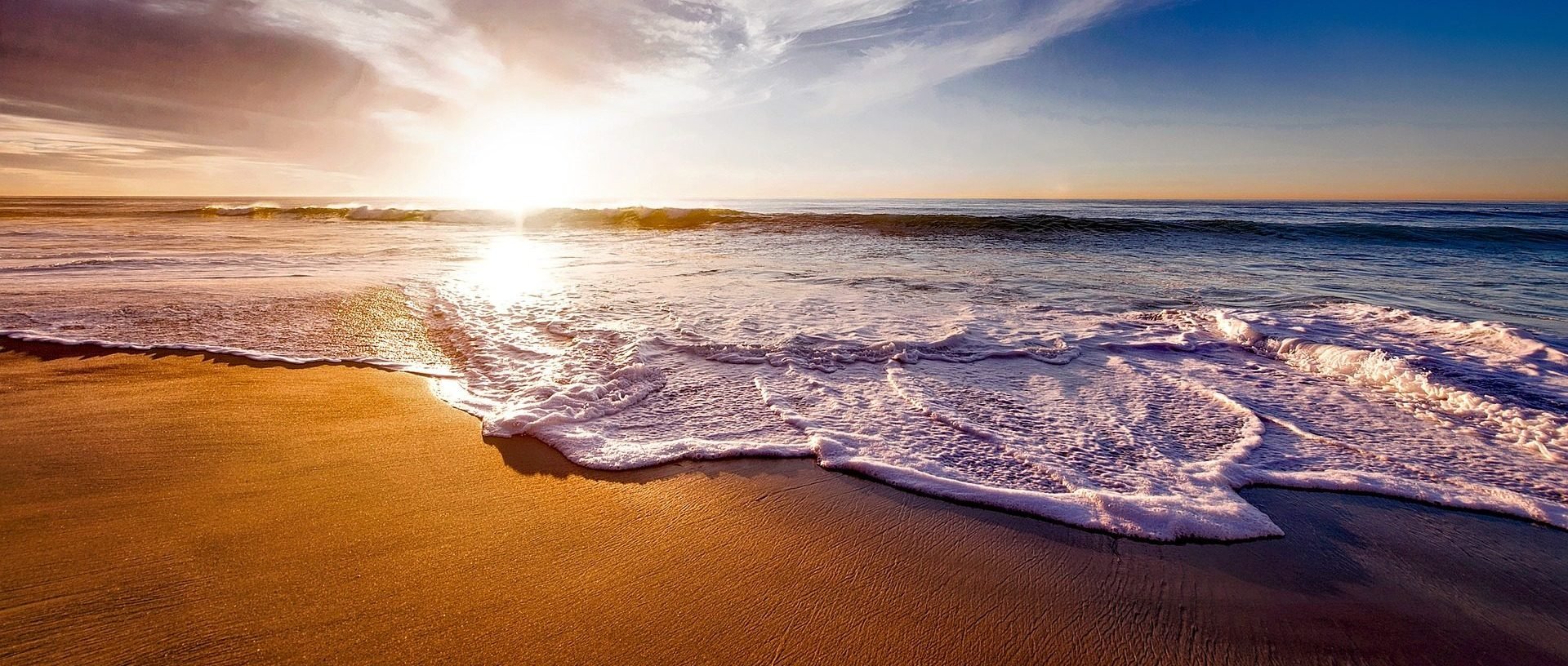 Sunset over the ocean with waves washing onto the sandy beach.