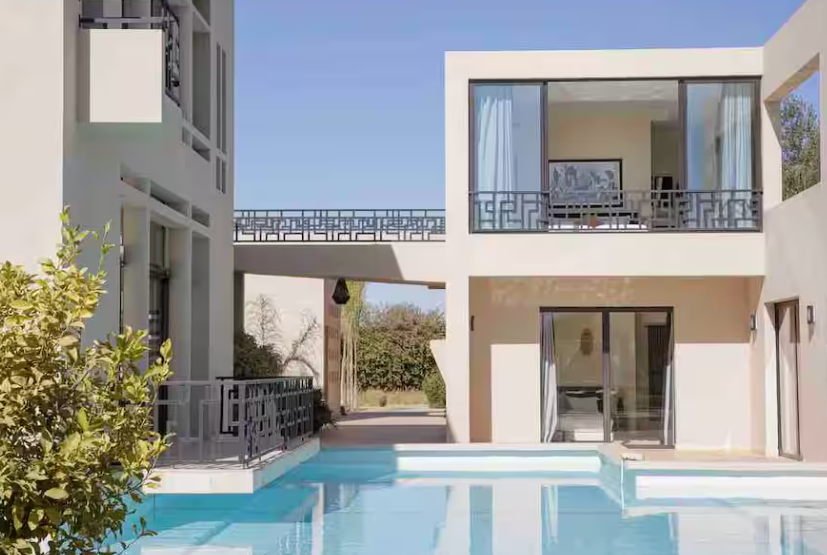 Modern white house with a swimming pool in front, two-story structure with large glass doors and windows, and a balcony with decorative railing.