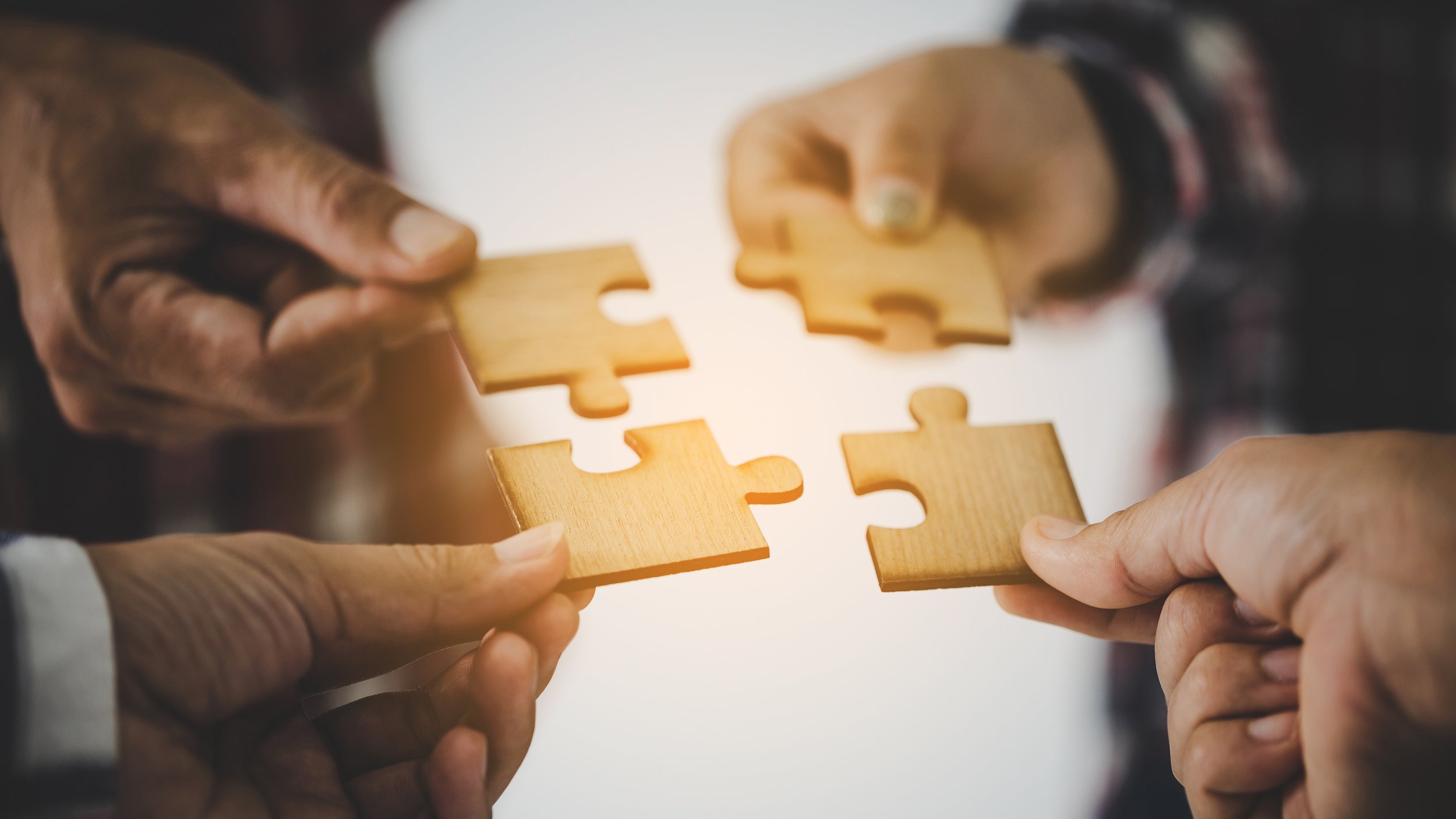 Multiple hands holding wooden jigsaw puzzle pieces, fitting them together.