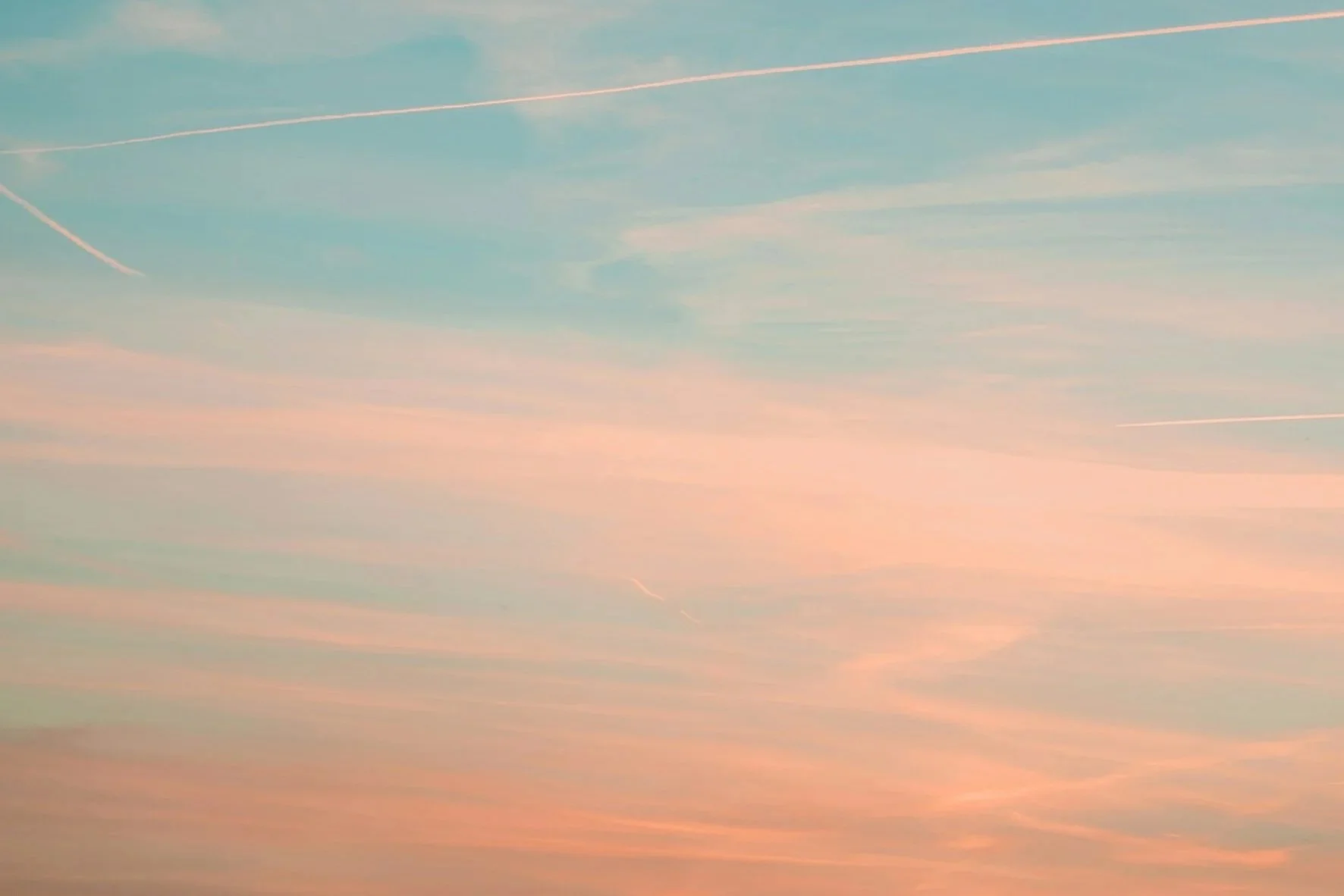 A sky with pastel-colored clouds and contrails from airplanes at sunset or sunrise.