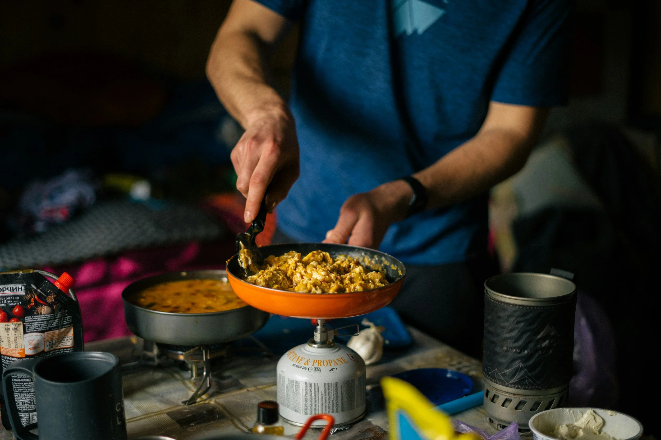 Person cooking a warm meal in a cast iron pan, representing food as community and nourishment