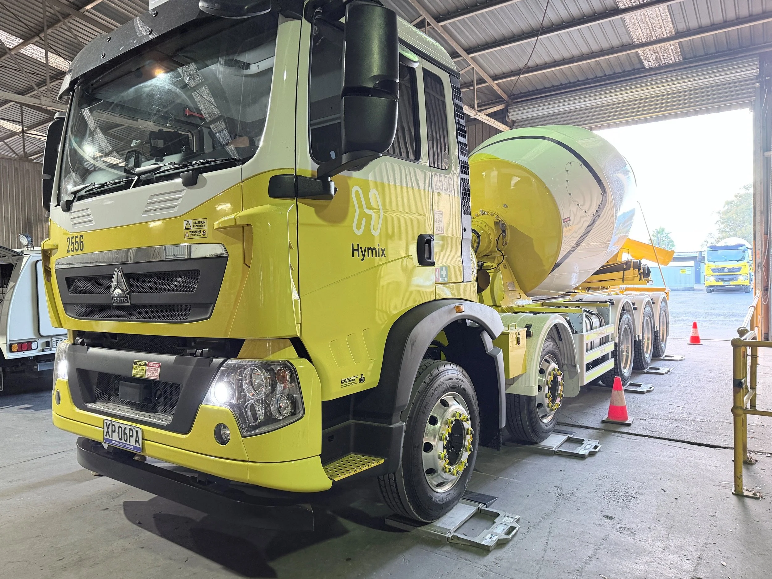 A large yellow cement mixer truck parked inside a warehouse, with the mixer drum visible on the back and vehicle parts supported on metal stands.