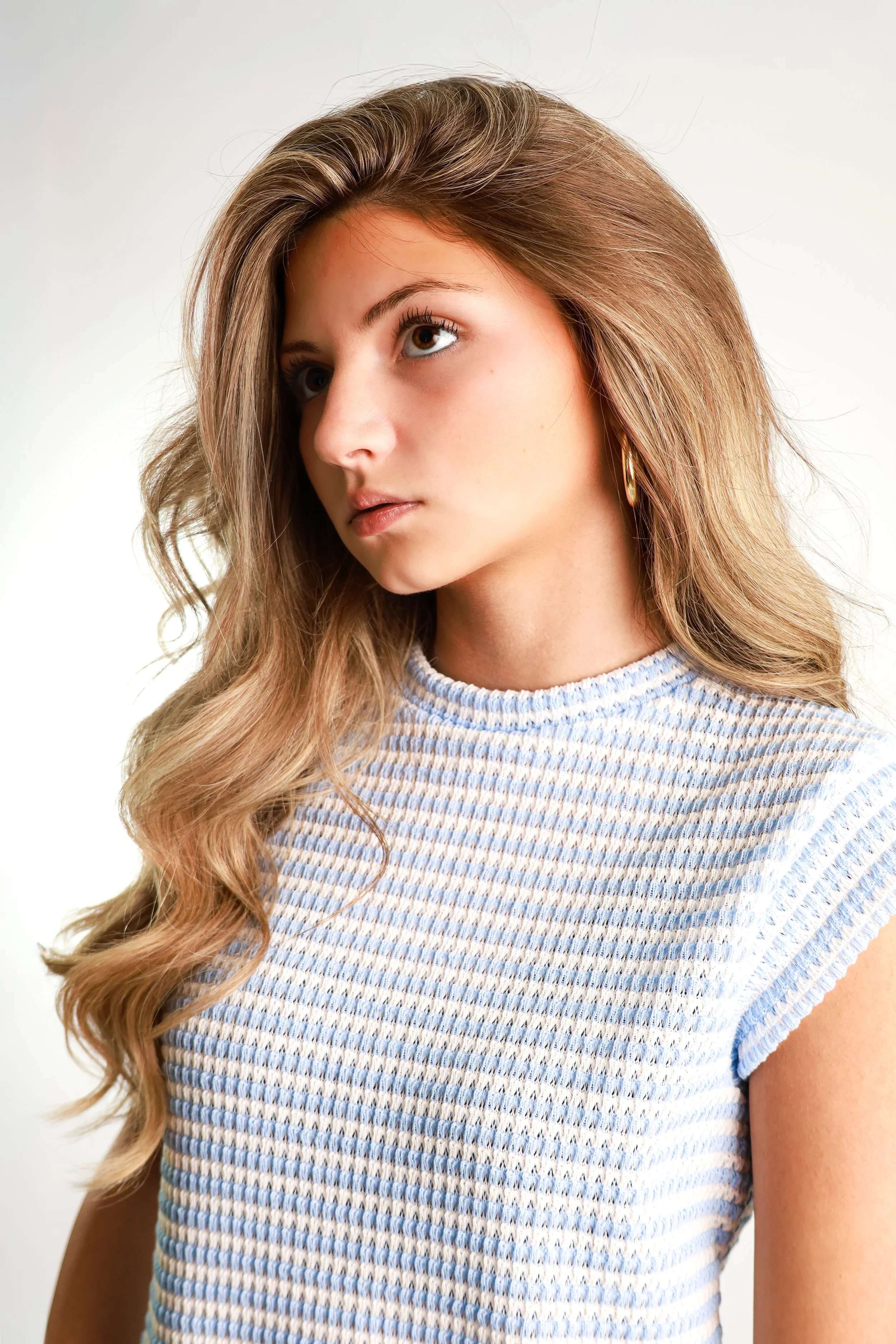Close-up of a woman with long wavy hair wearing a striped shirt, looking to the side.