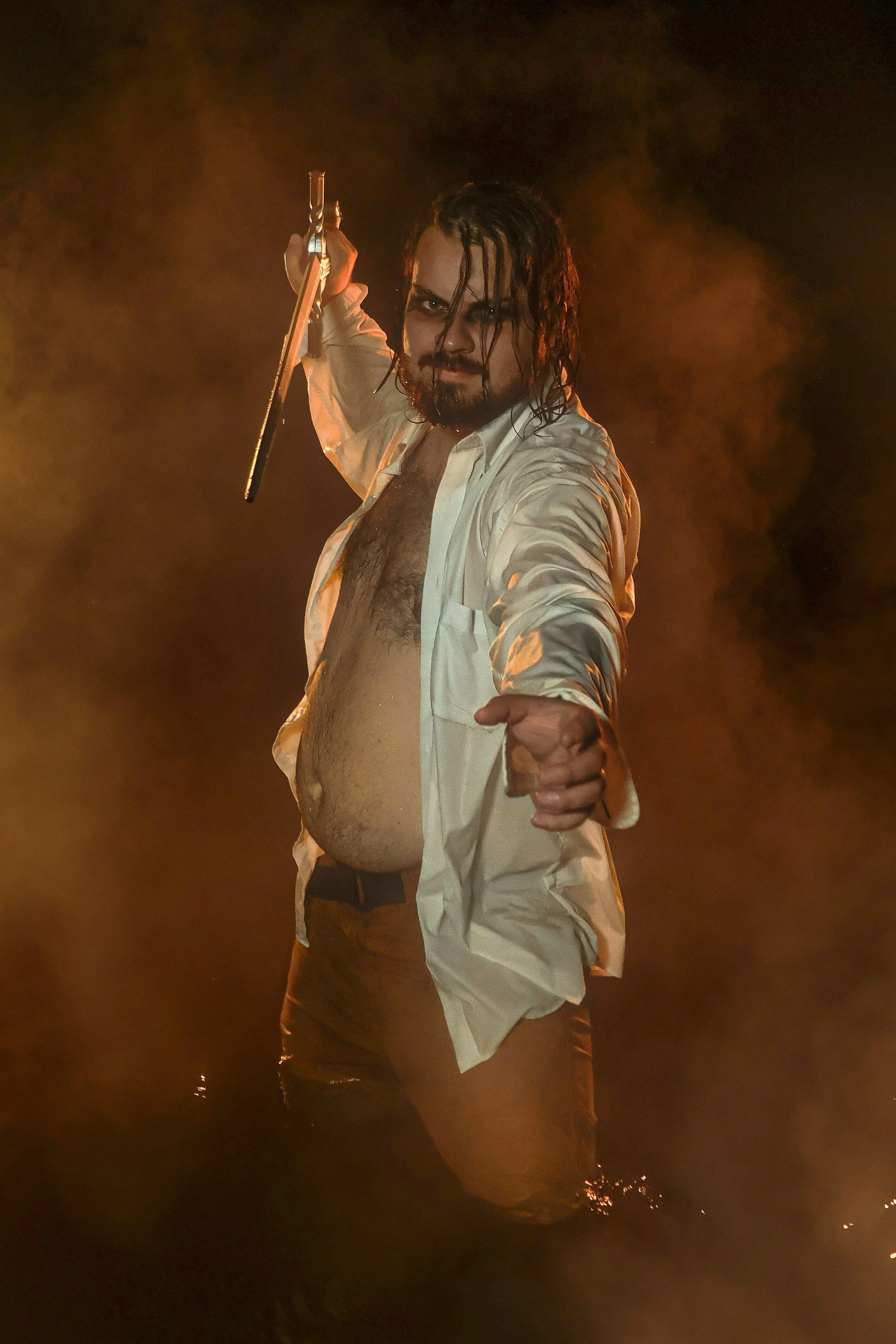 A man with long, dark, wet hair and a beard, dressed in an open white shirt revealing his chest, holding a sword over his shoulder, standing in a smoky, dimly lit environment.