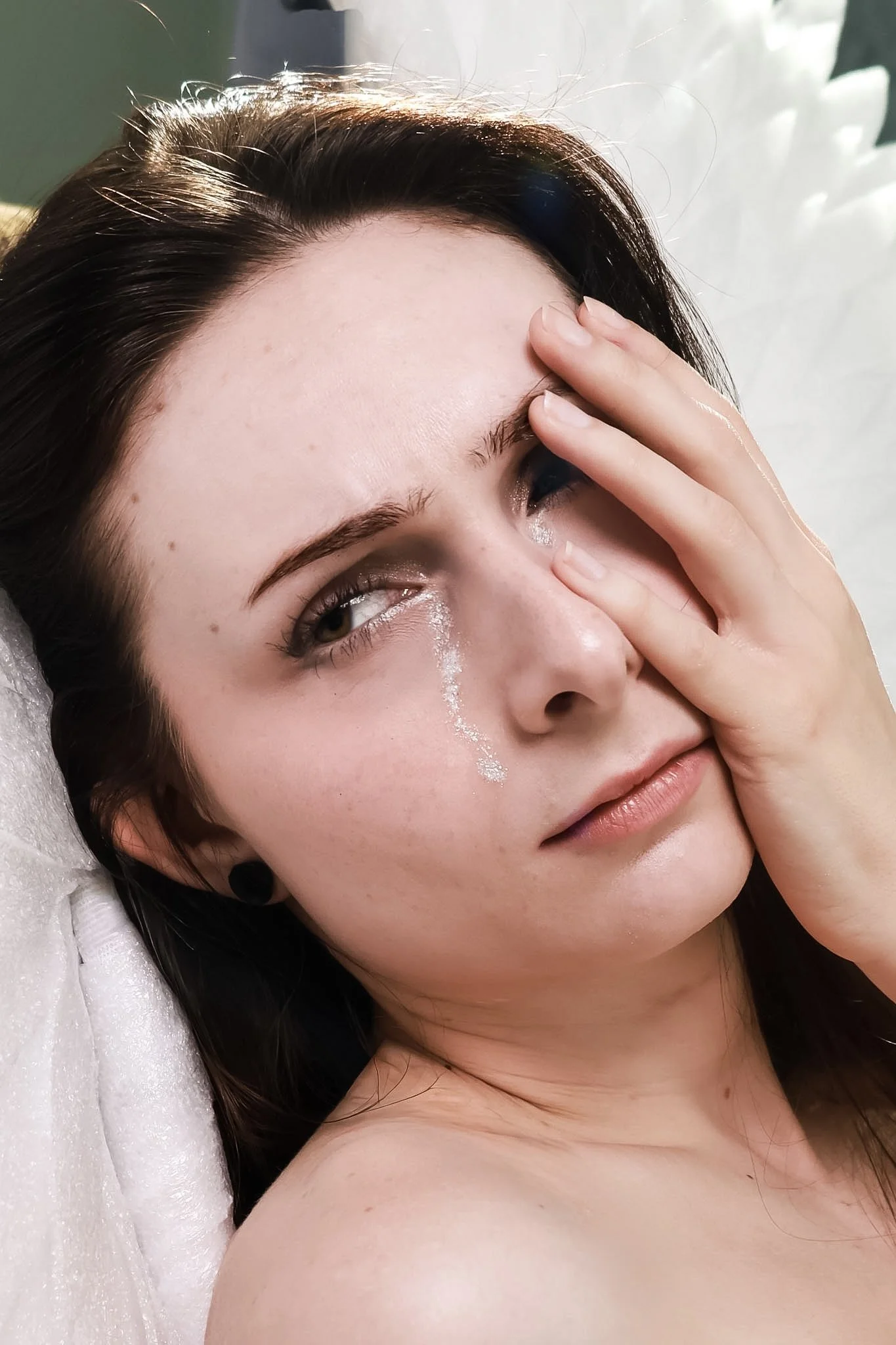 Close-up of a woman lying down with her eyes closed, touching her forehead with her fingers, and a visible tear streak on her cheek.