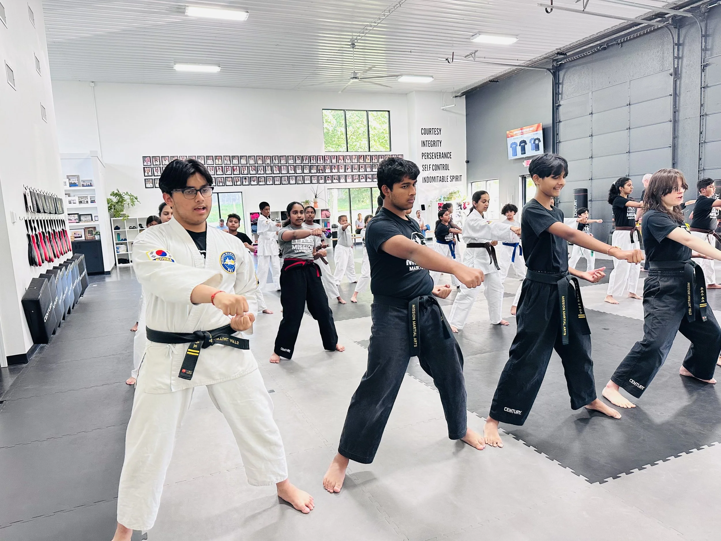 Group of martial arts students practicing martial arts in a training studio, wearing gi uniforms and black belts, with some instructors guiding them.