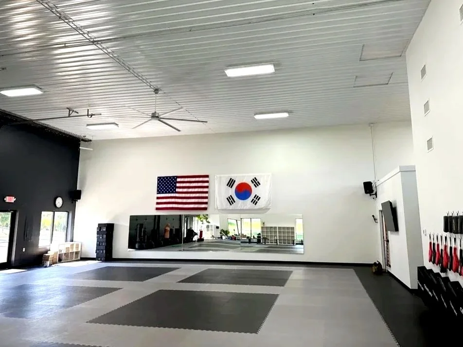 Empty martial arts training room with flags of the United States and South Korea, mirrors, and martial arts equipment.