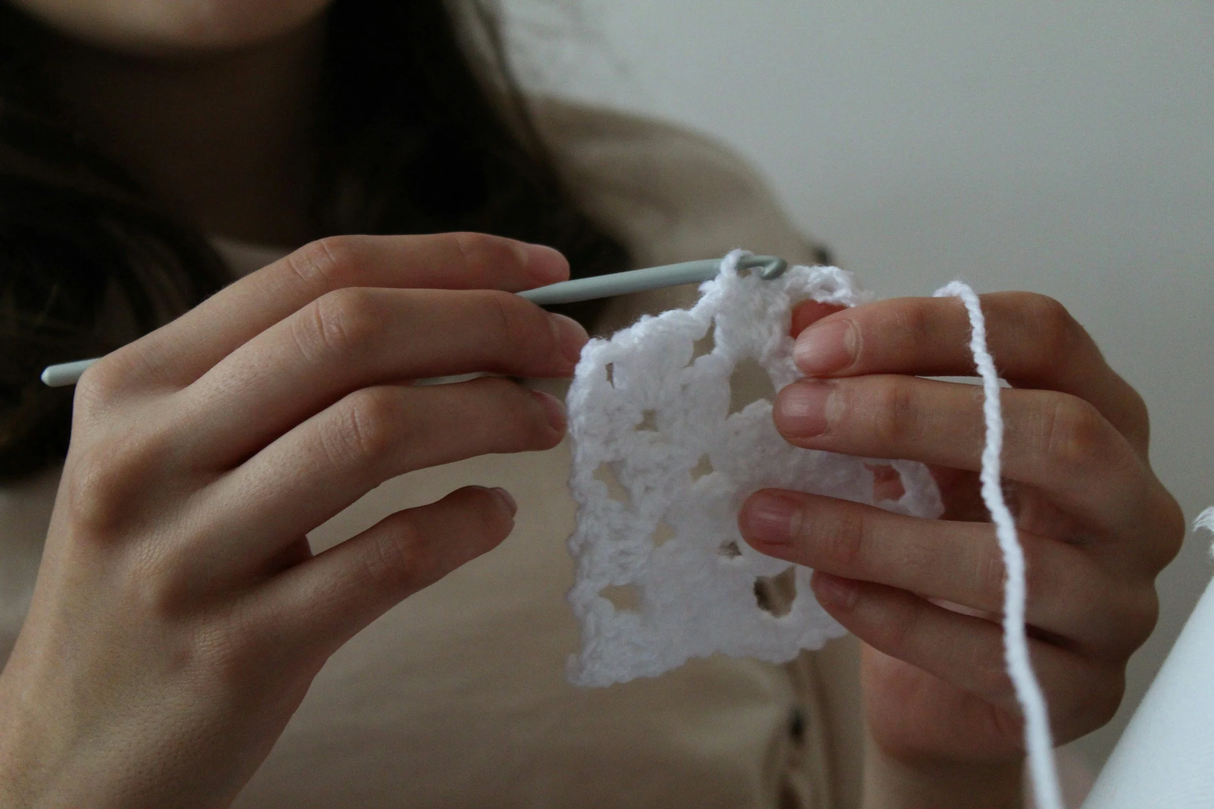 A person knitting with white yarn using a crochet hook.