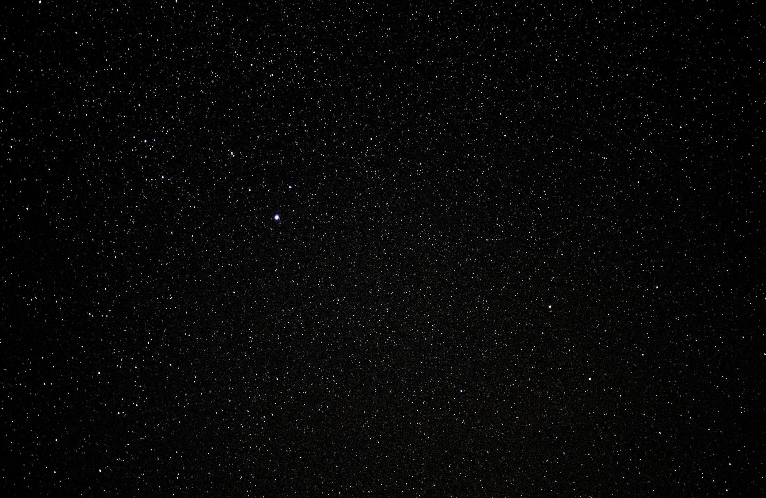 A clear night sky filled with numerous small stars and a few brighter stars or planets.