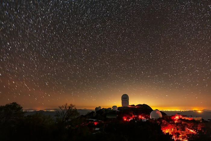 The Mayall 4-meter Telescope dome on Kitt Peak at night, with Tucson’s light pollution glowing on the horizon behind it.