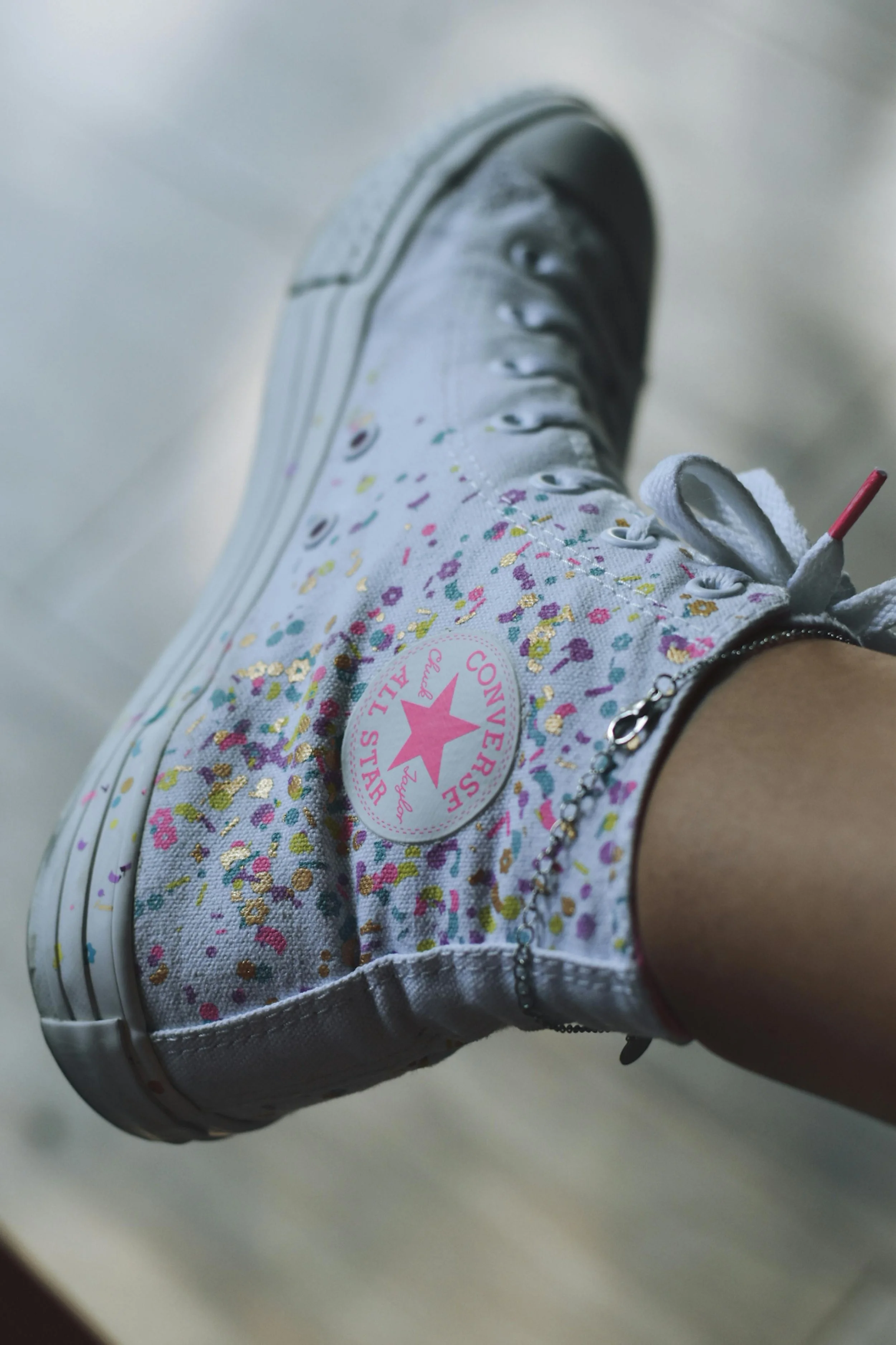 A person wearing white Converse sneakers with colorful floral pattern, taken from a low angle, focusing on the shoe.