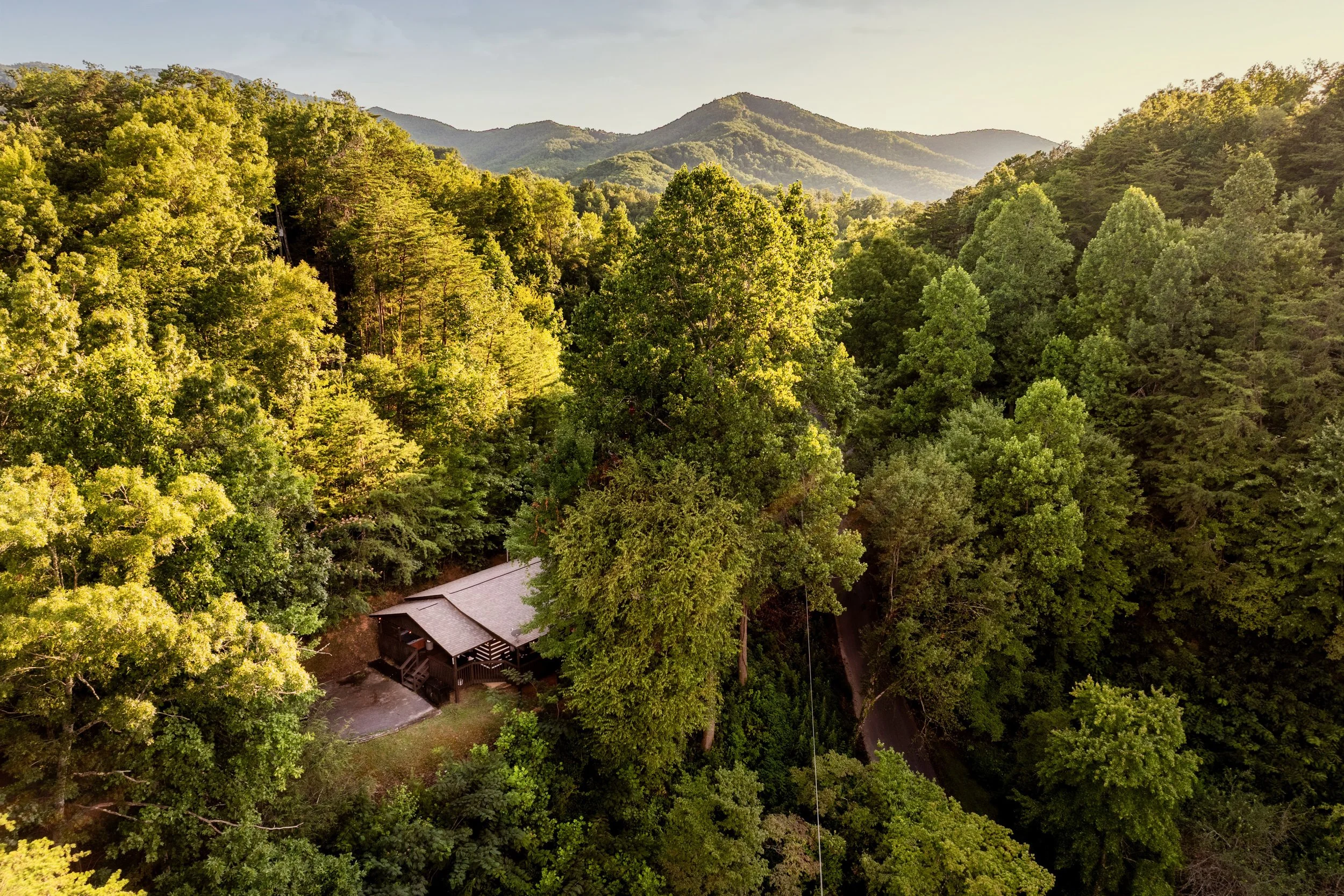 Aerial view of a densely forested mountainous landscape with a building at the bottom.