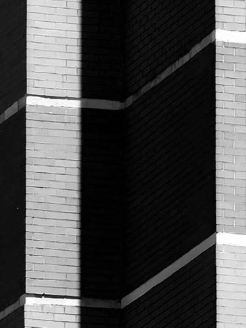 Close-up of a brick building corner with shadows and white mortar lines.