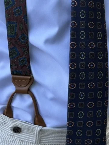 Close-up of a mannequin with a white shirt, patterned suspenders, and a dark-colored tie with geometric designs.