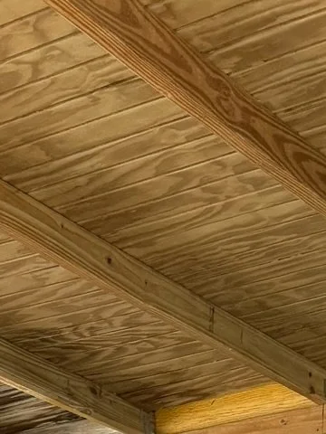 Close-up view of wooden ceiling beams and tongue-and-groove wooden panels.