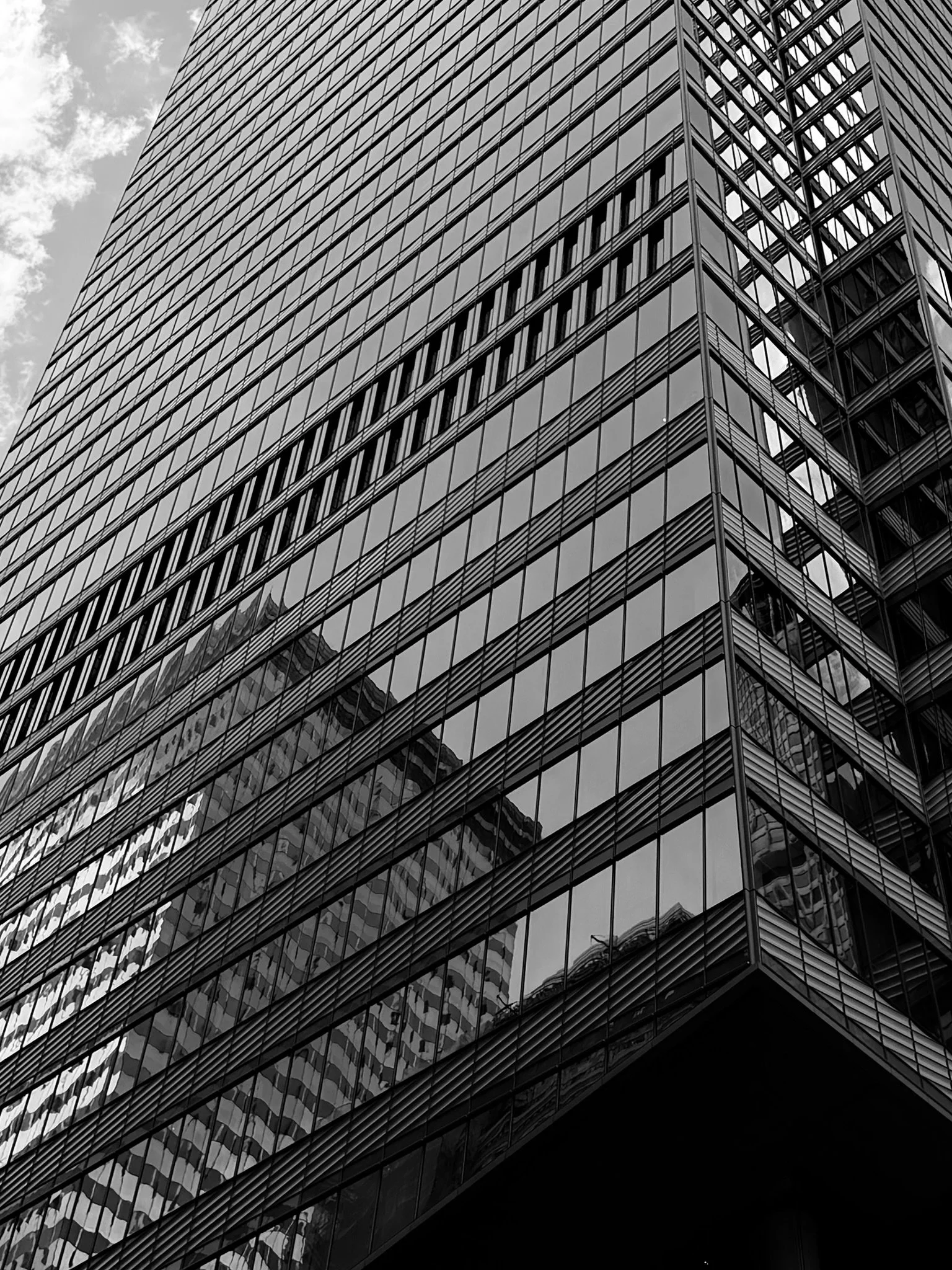 A black and white photo of a modern glass skyscraper showing its angled façade and reflective windows.